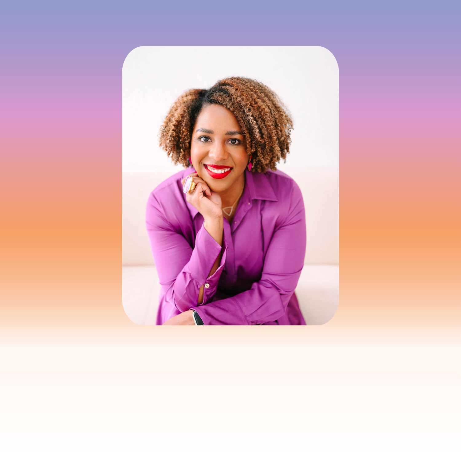 A woman with curly, shoulder-length hair, wearing a purple blouse, smiling and resting her chin on her hand, against a plain white background.