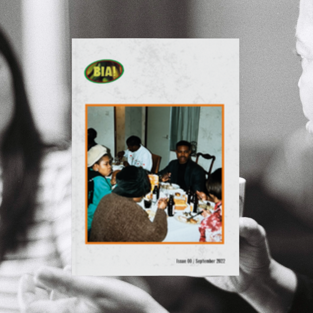 A group of people are sitting around a table enjoying a meal at a gathering or celebration. The table has bottles and food on it, and the room has light-colored walls and curtains. The image is part of Bia! Zine issue 1's cover.