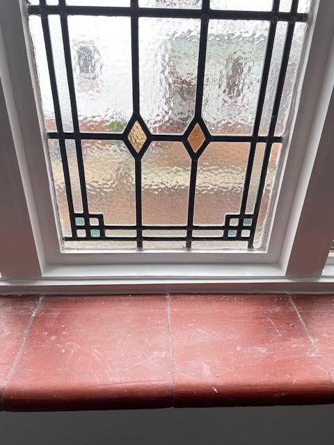 Stained glass window with geometric patterns above a red tiled windowsill.
