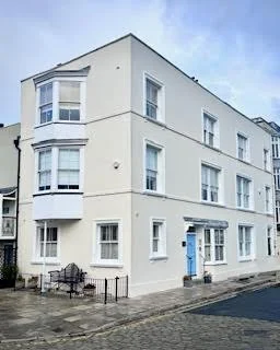 A white corner apartment building with multiple windows, situated on a city street with a cloudy sky.