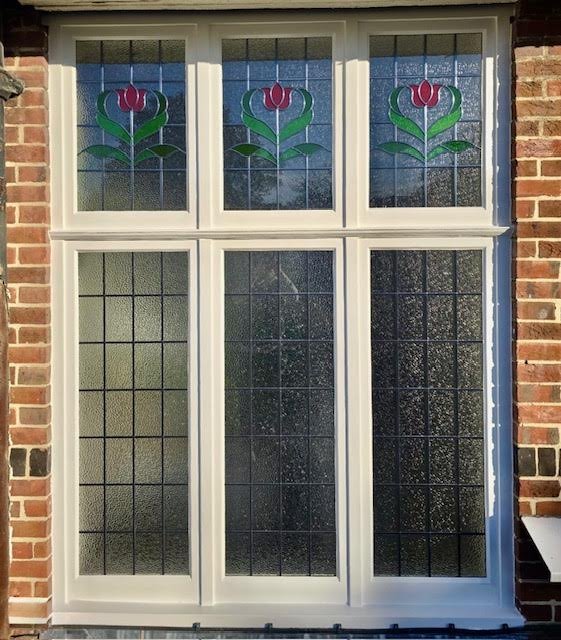 Decorative stained glass window with red and green floral design at the top, set in a white frame on a brick wall.