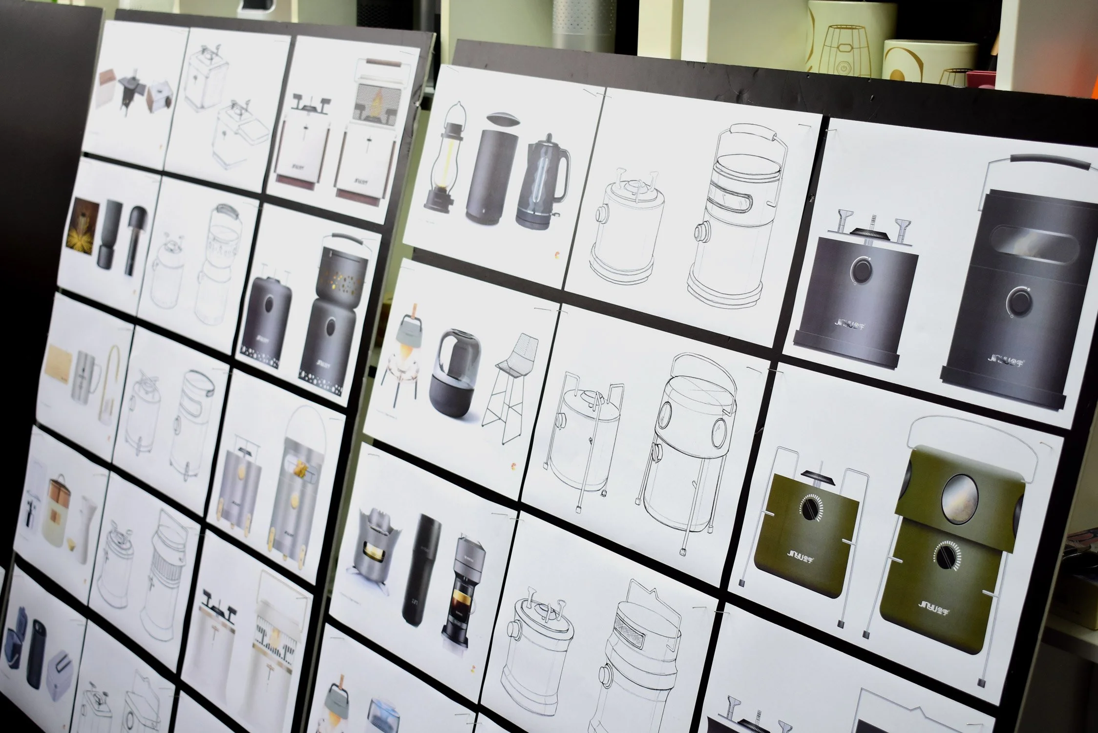 Display of technical sketches and designs for small household appliances such as vacuum cleaners and humidifiers, arranged on illuminated boards in a store or design studio.