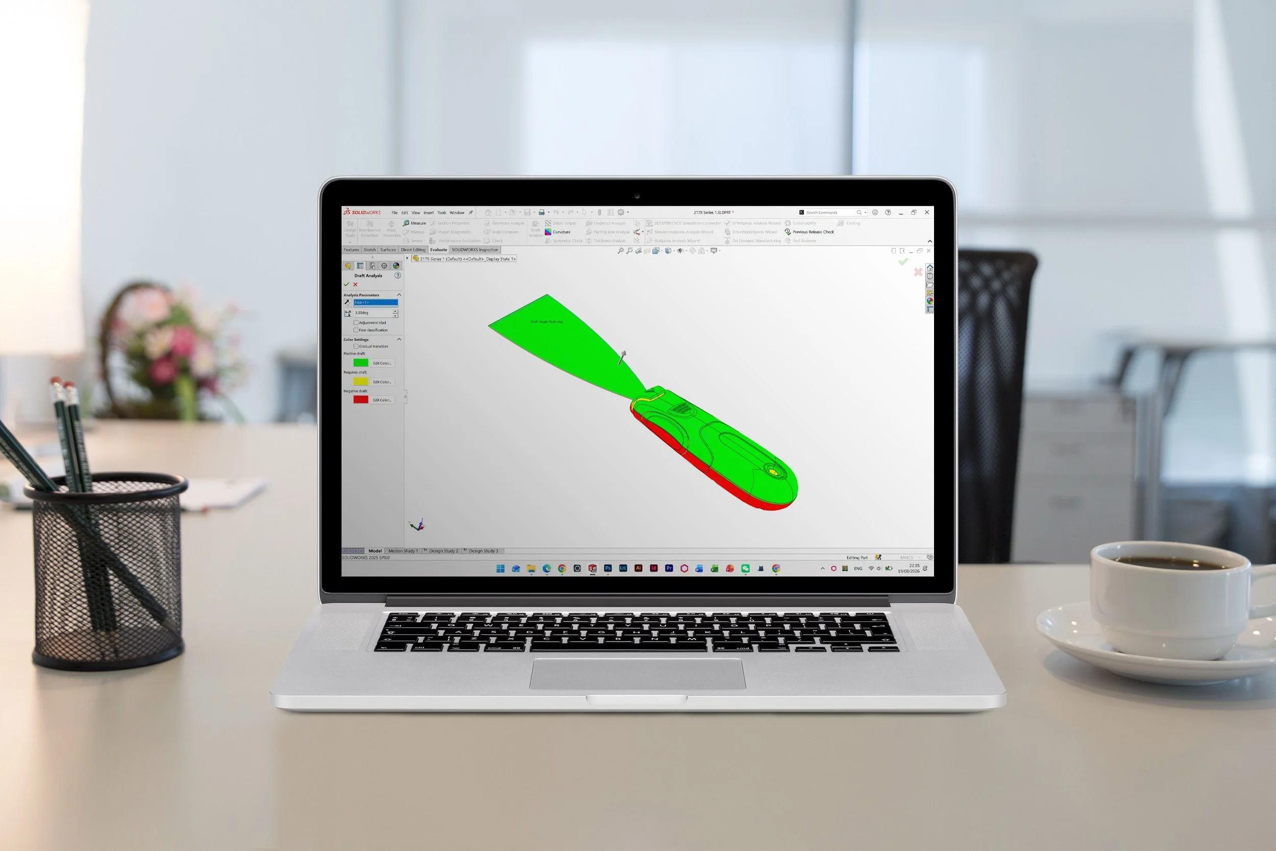 Laptop on a white desk displaying a 3D modeling software with a model of a car in green and red colors, in a modern office environment with a blurred background.