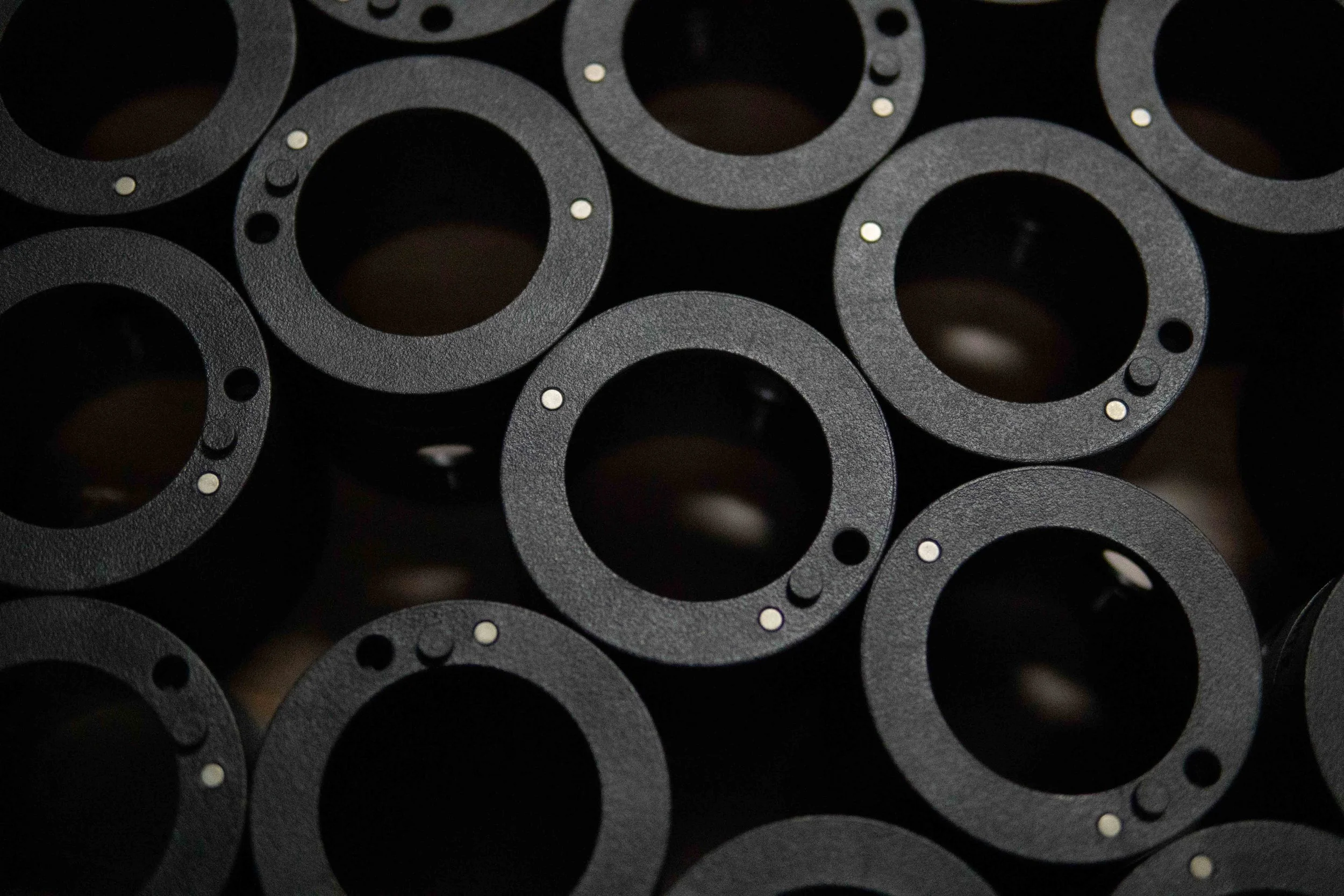 A close-up image of multiple black, circular rubber or plastic washers or gaskets with small metallic inserts or pins in the center of each.