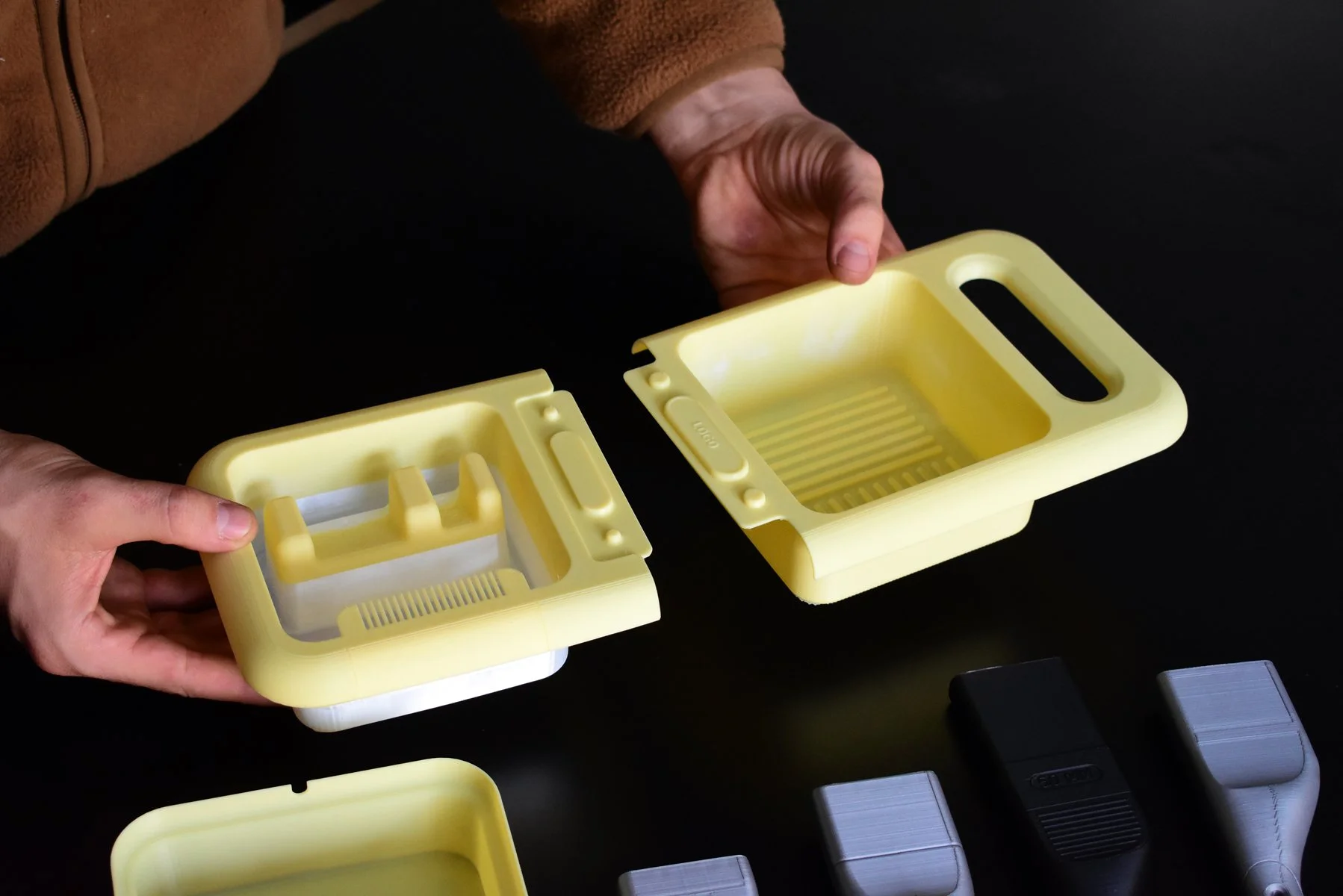 A person holding two yellow plastic objects with slots, likely used for organizing or storage, against a dark background with other objects partially visible.