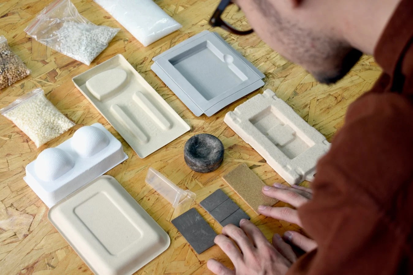 Person examining various packaging materials, laboratory supplies, and samples on a wooden surface.