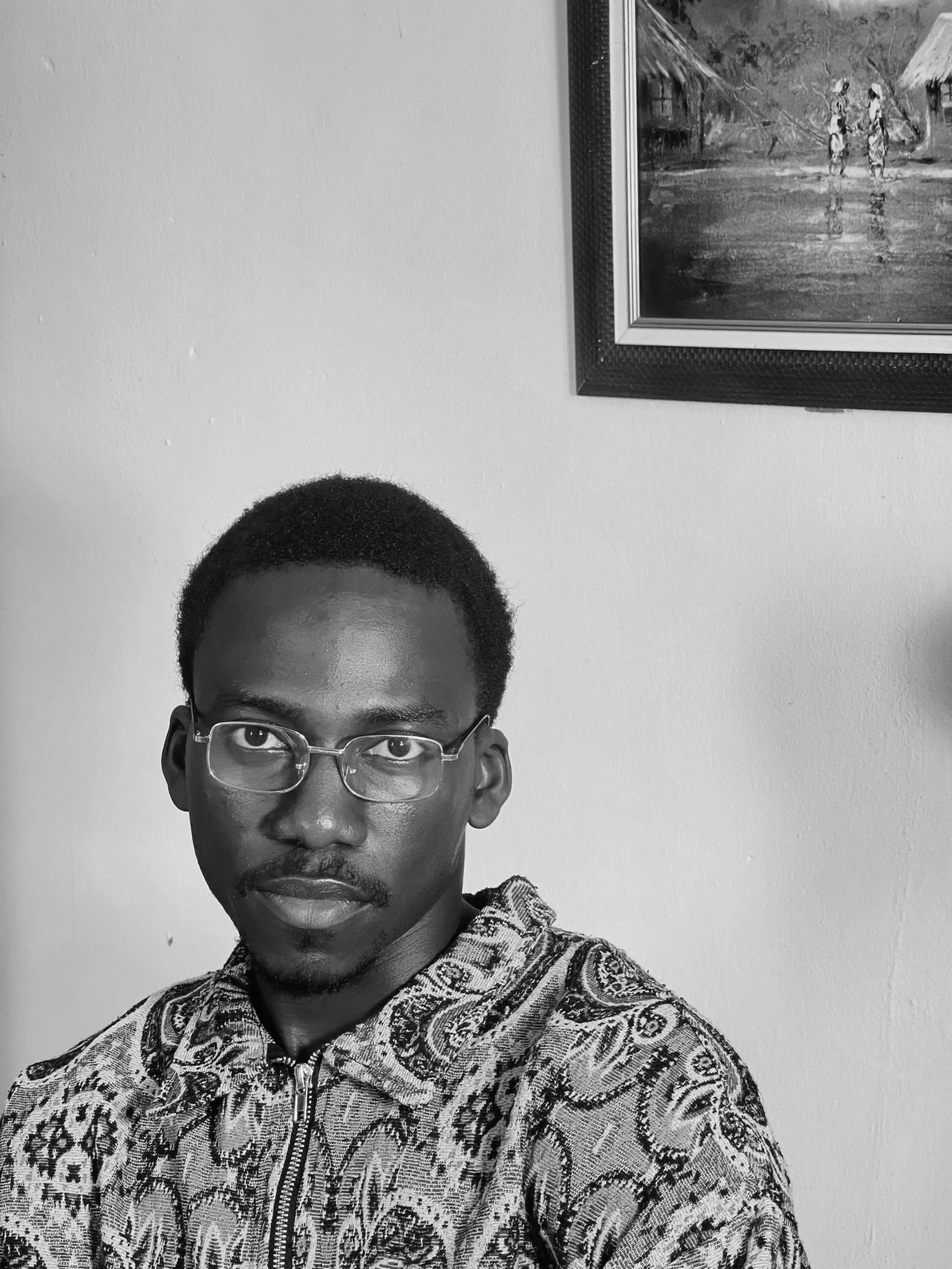 Young man wearing glasses posing in front of a portrait.