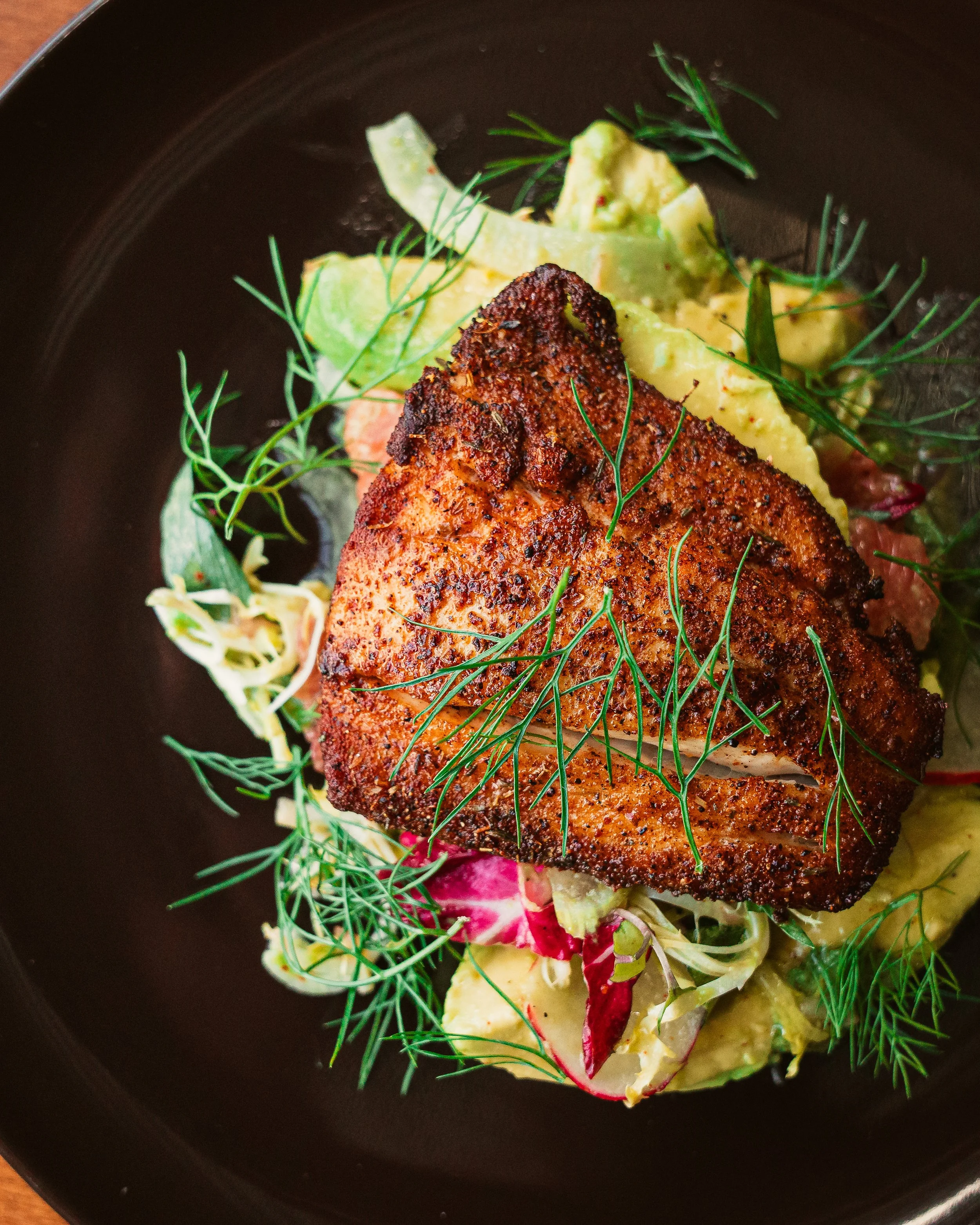 A seasoned, cooked piece of fish on a bed of salad greens, garnished with fresh dill.