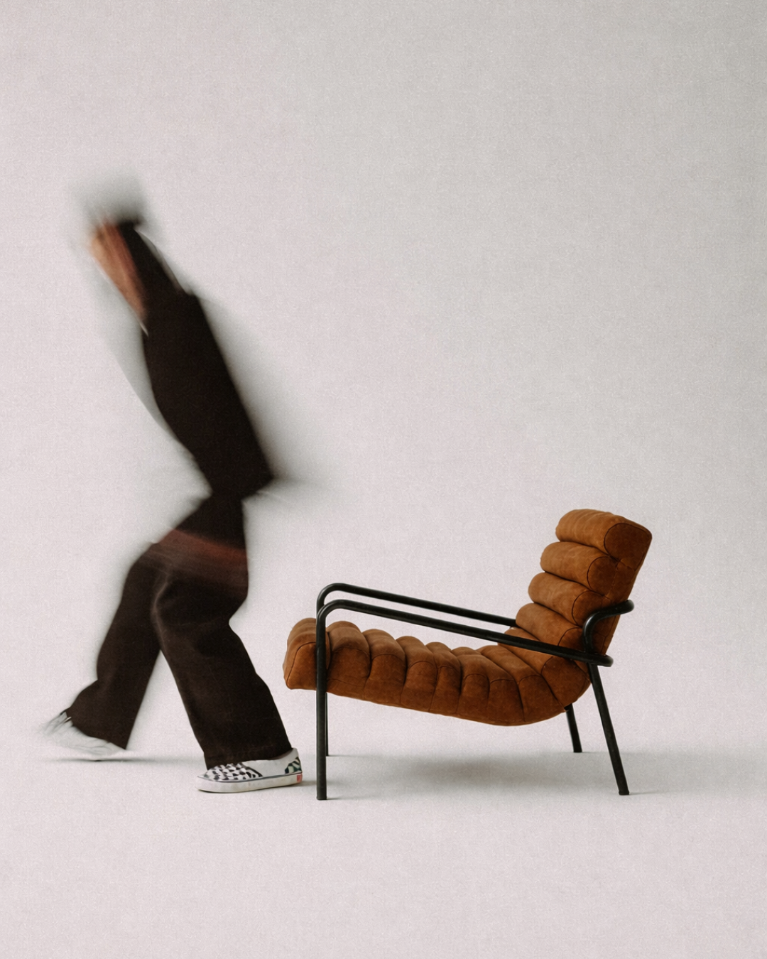 Abstract photography of upholstered chair with black metal frame, against a plain white background with person moving.