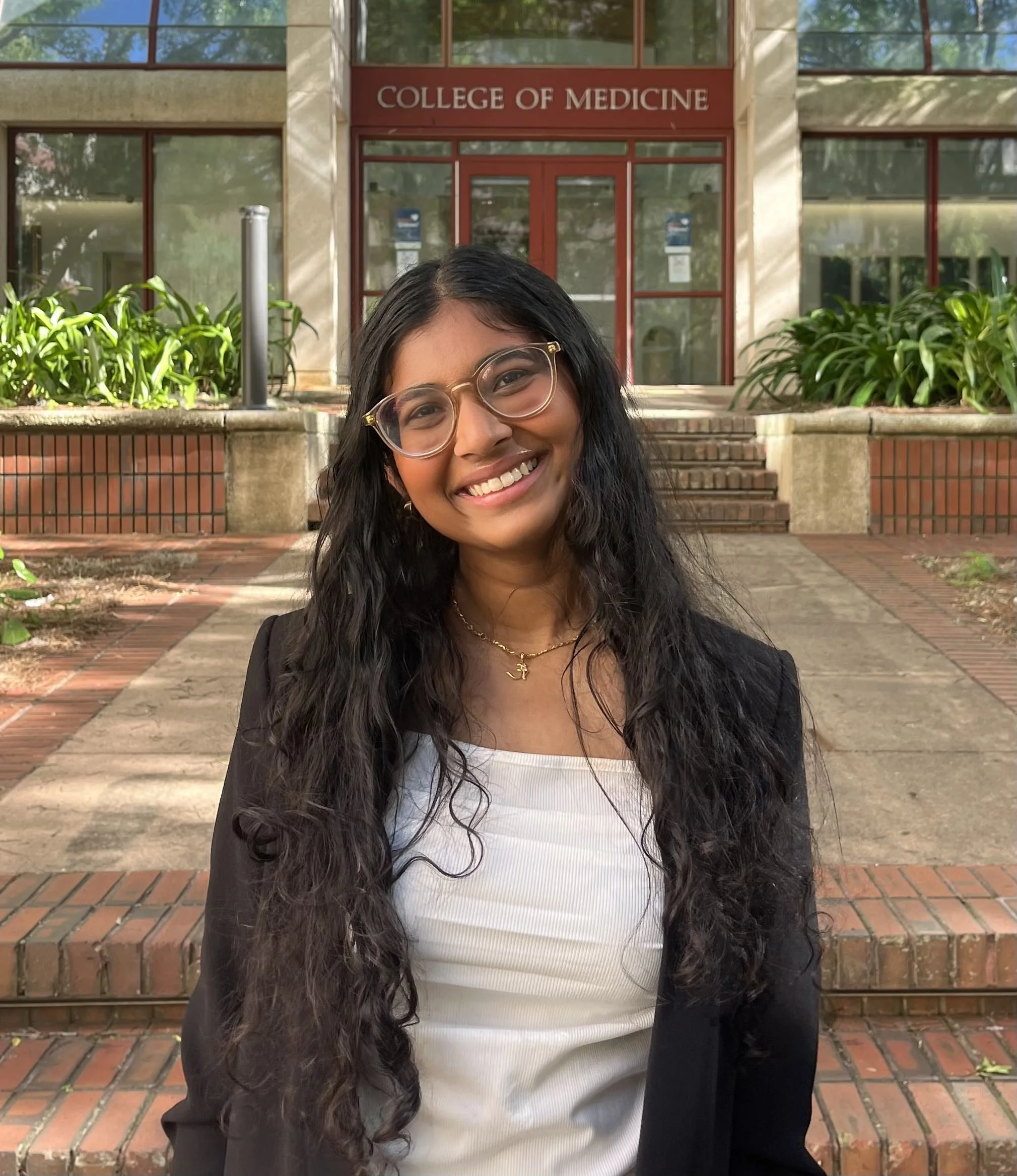 Photo of a young woman with long dark hair smiling in front of the College of Medicine building