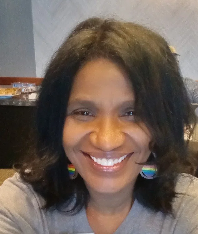 Photo of a woman smiling and wearing rainbow earrings