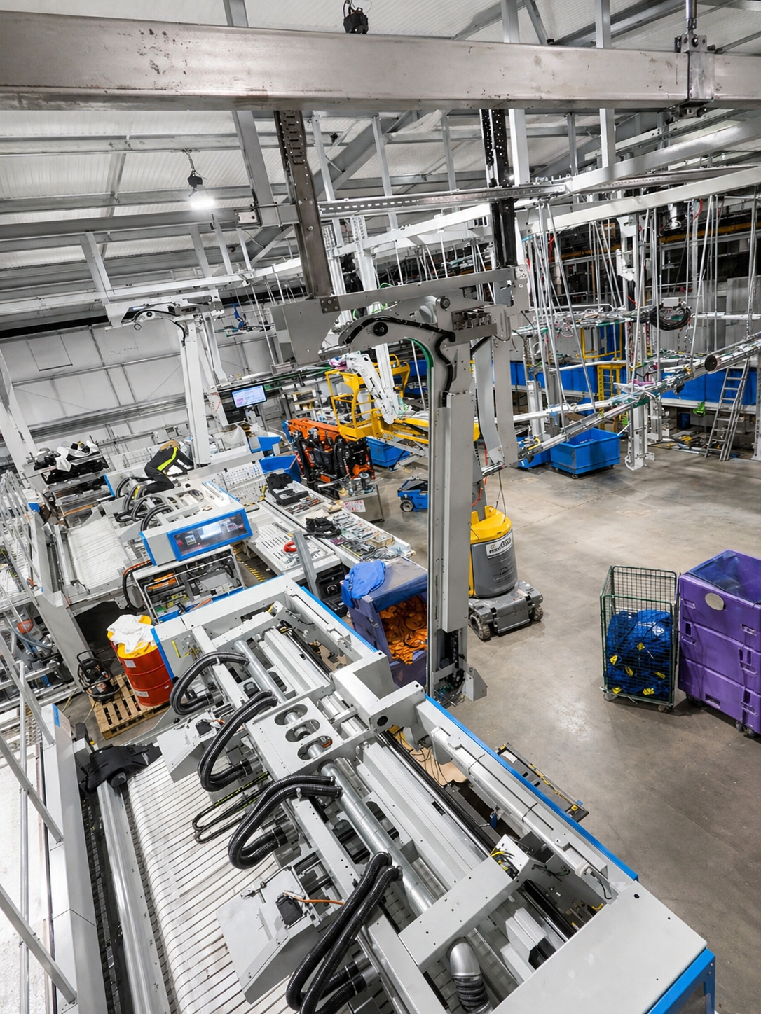 Industrial manufacturing facility with robotic machinery, conveyor systems, workstations, storage bins, and various tools.