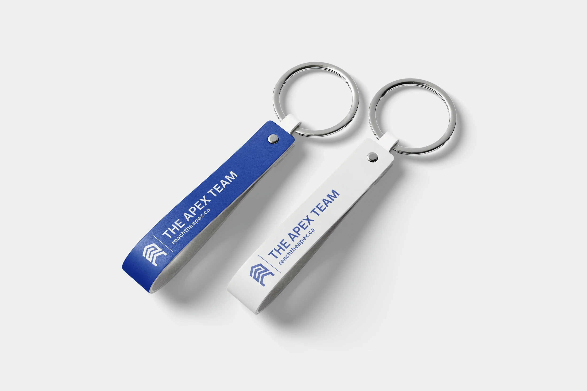 Two Apex Team branded metal keychains with logo and brand name — real estate promotional merchandise designed by So Very Madly.