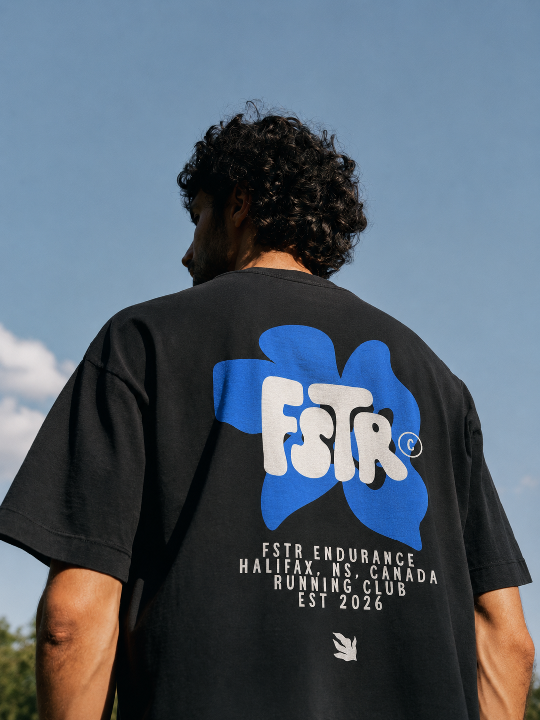 FSTR Endurance limited-edition floral logo on a black T-shirt — specialty brand identity design featuring the FSTR wordmark set inside an electric-blue organic floral graphic, worn on a running club member.