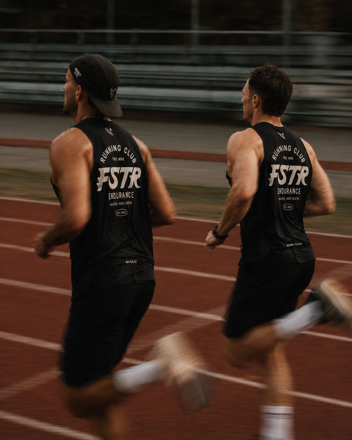 FSTR Endurance Running Club brand identity on apparel — two runners sprinting on a track wearing matching black FSTR Endurance muscle shirts, demonstrating the logo in motion.