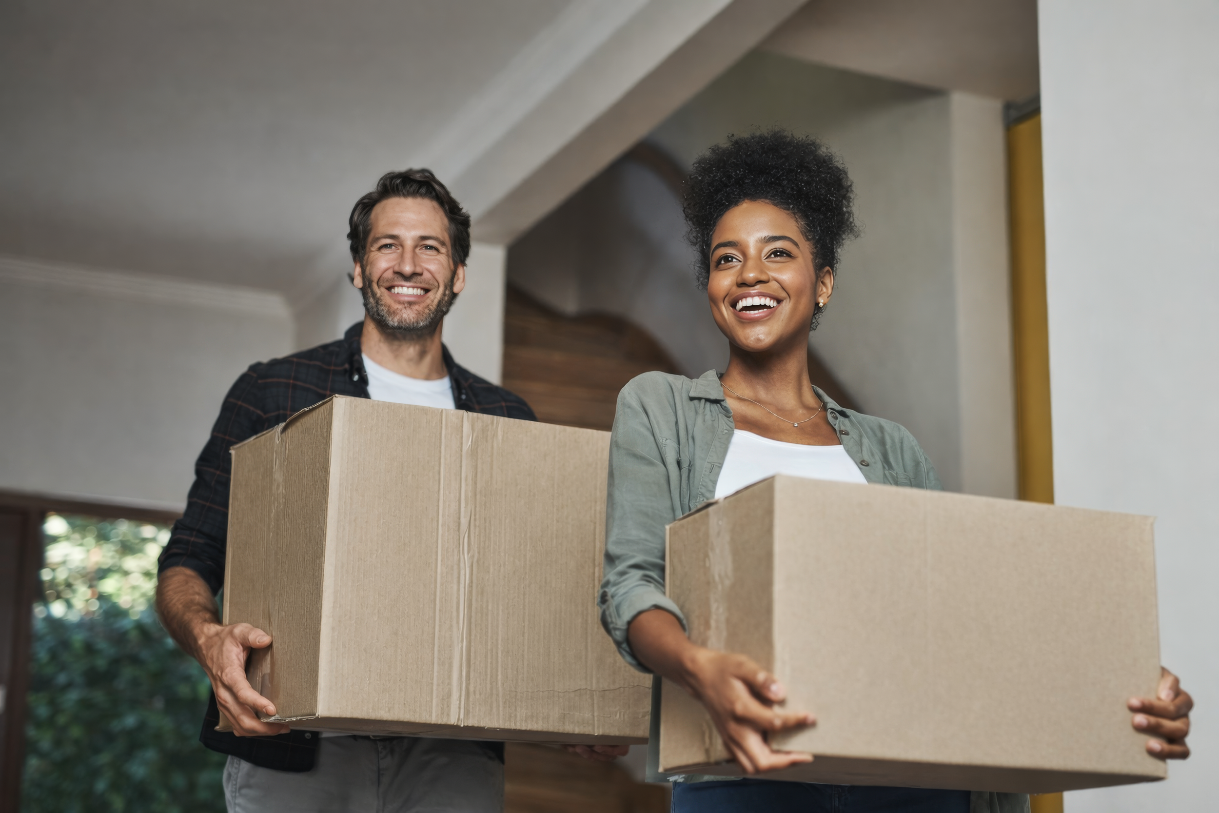 Smiling couple carry moving boxes together — lifestyle photography representing The Apex Team's warm, human approach to real estate.