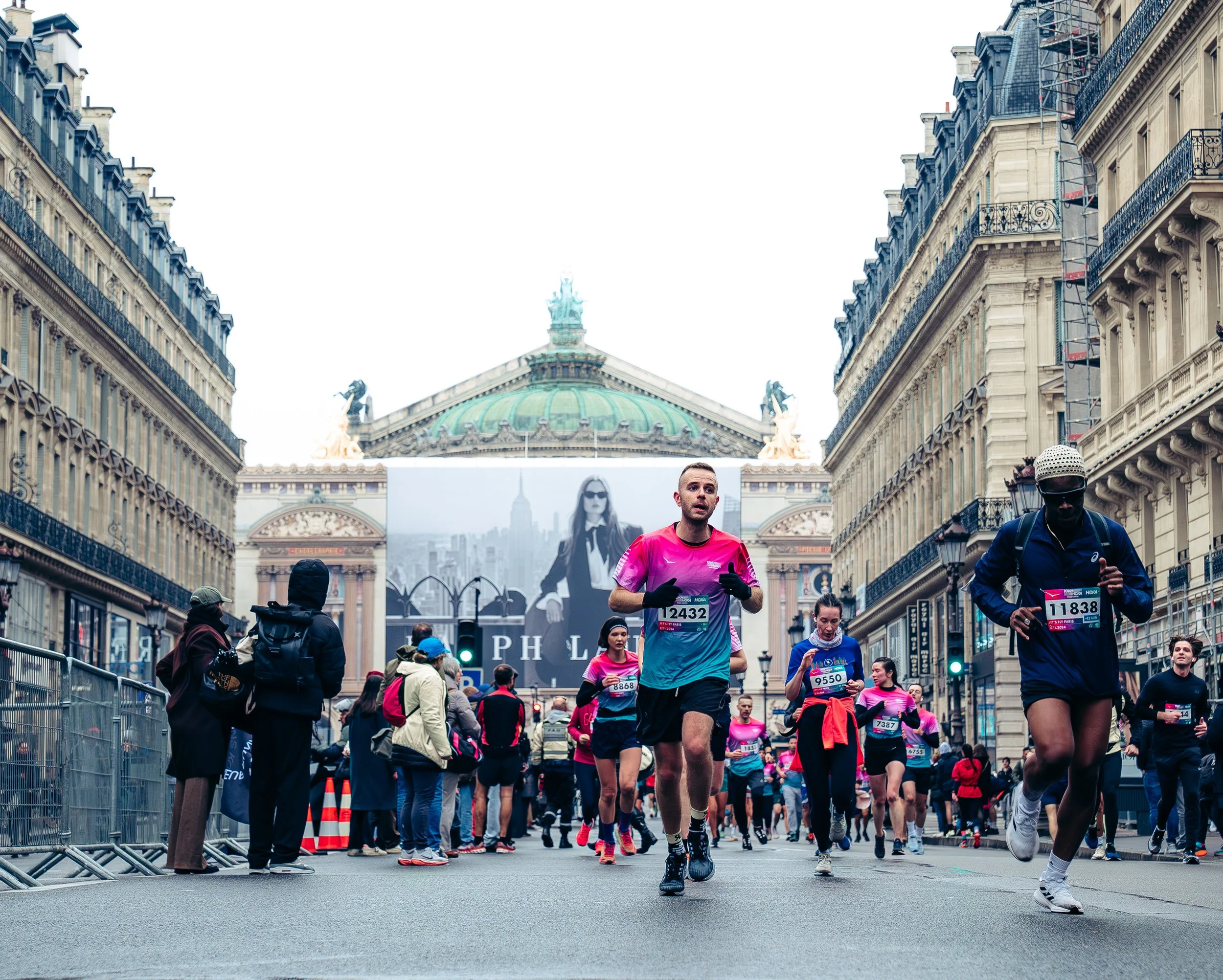 Marathon runners in a city street race with a historic building and large billboard in the background.