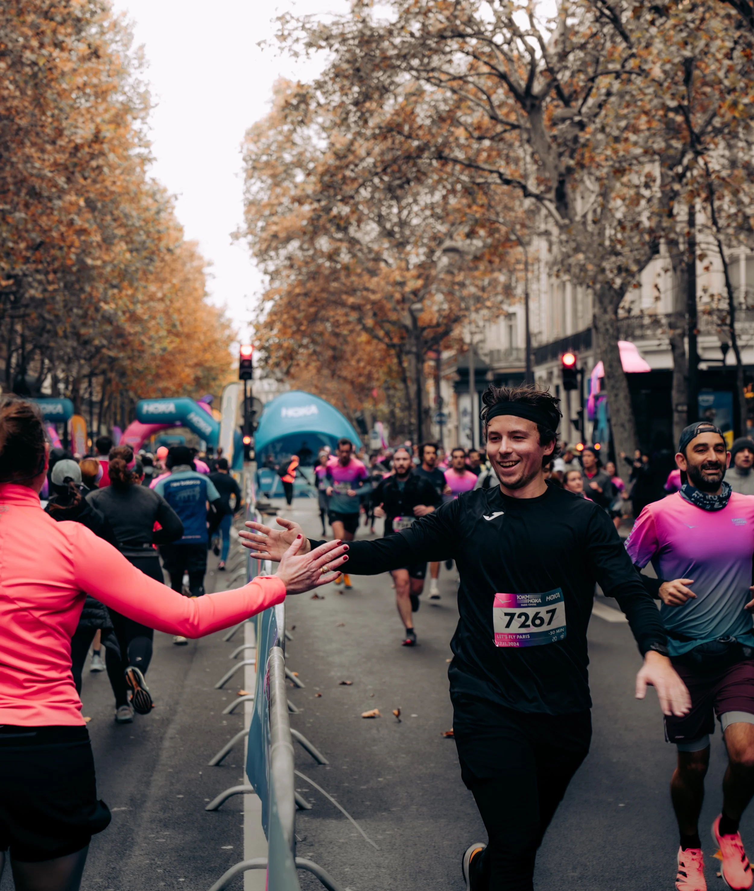 People participating in a marathon race, some are reaching a finish line, with trees and buildings in the background on a city street.