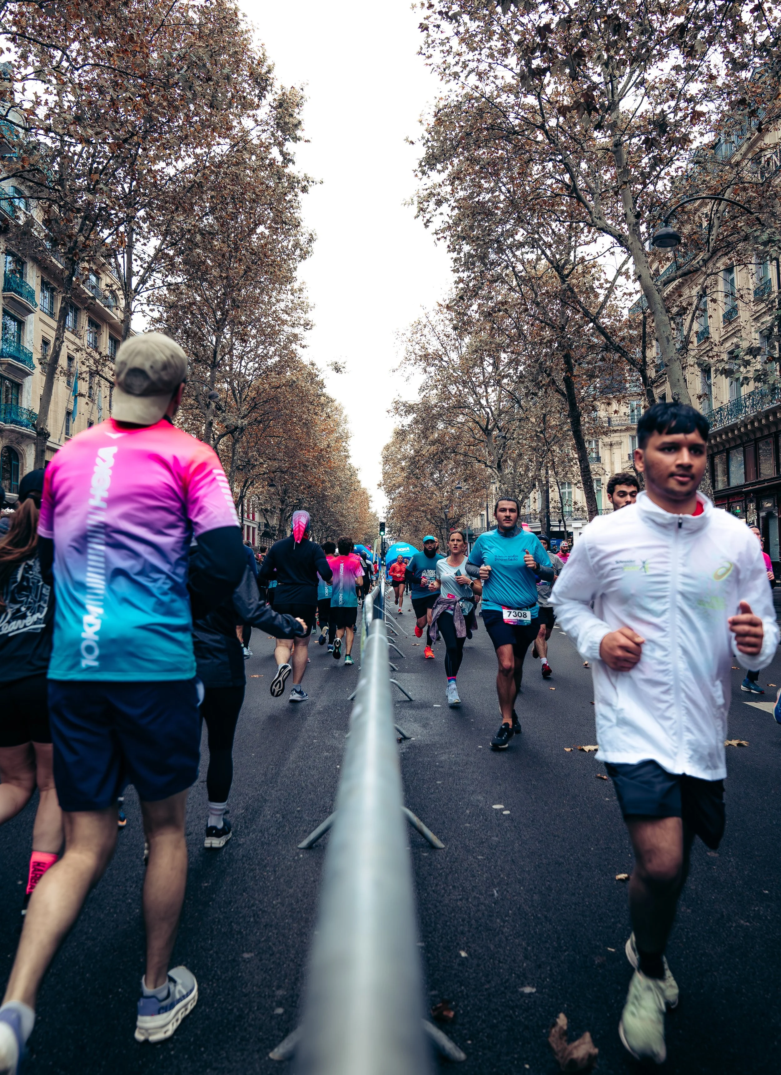 People running in a marathon on a city street lined with trees and buildings.