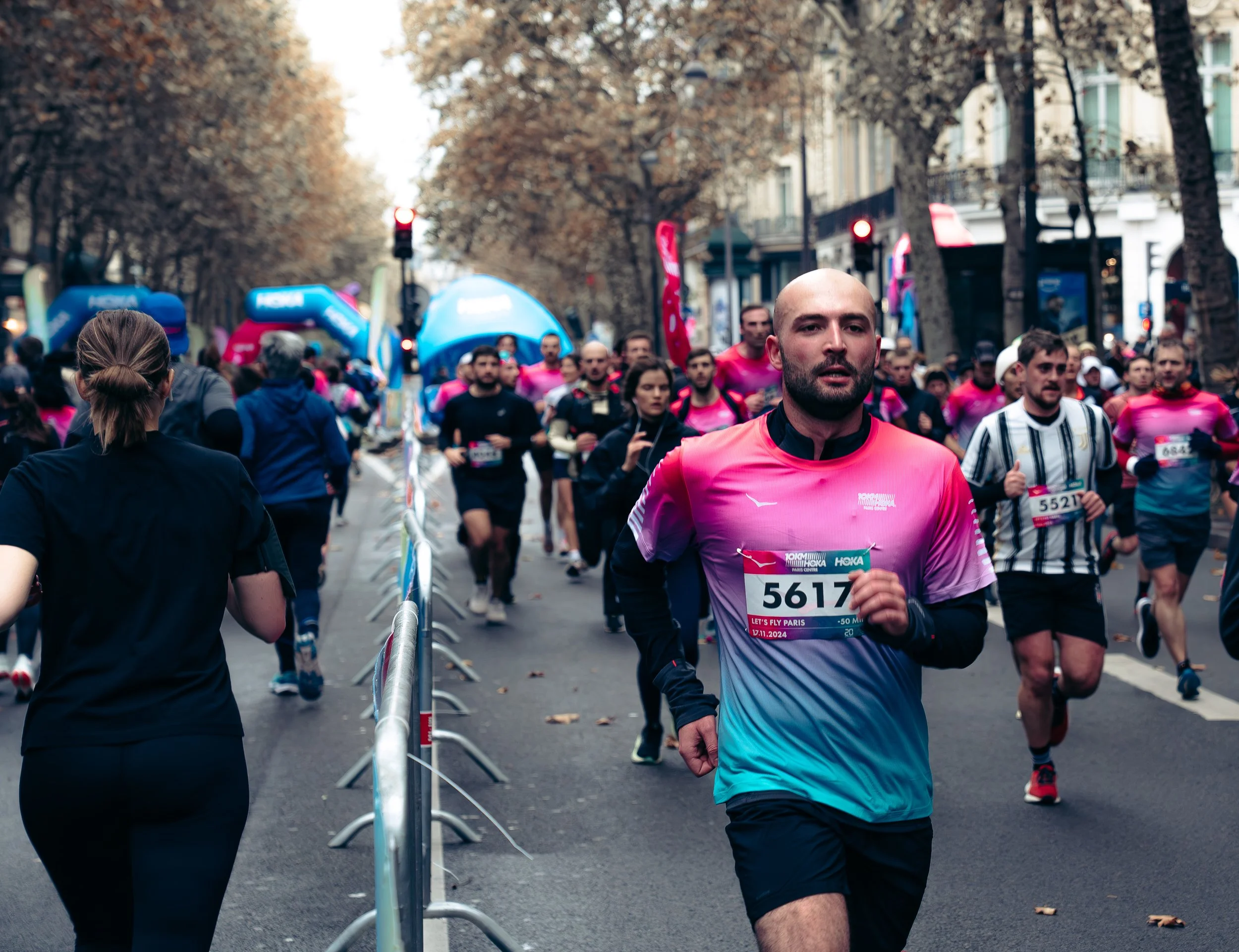 Marathon runners participating in a race on a city street with autumn-colored trees, with people and spectators along the sidelines.