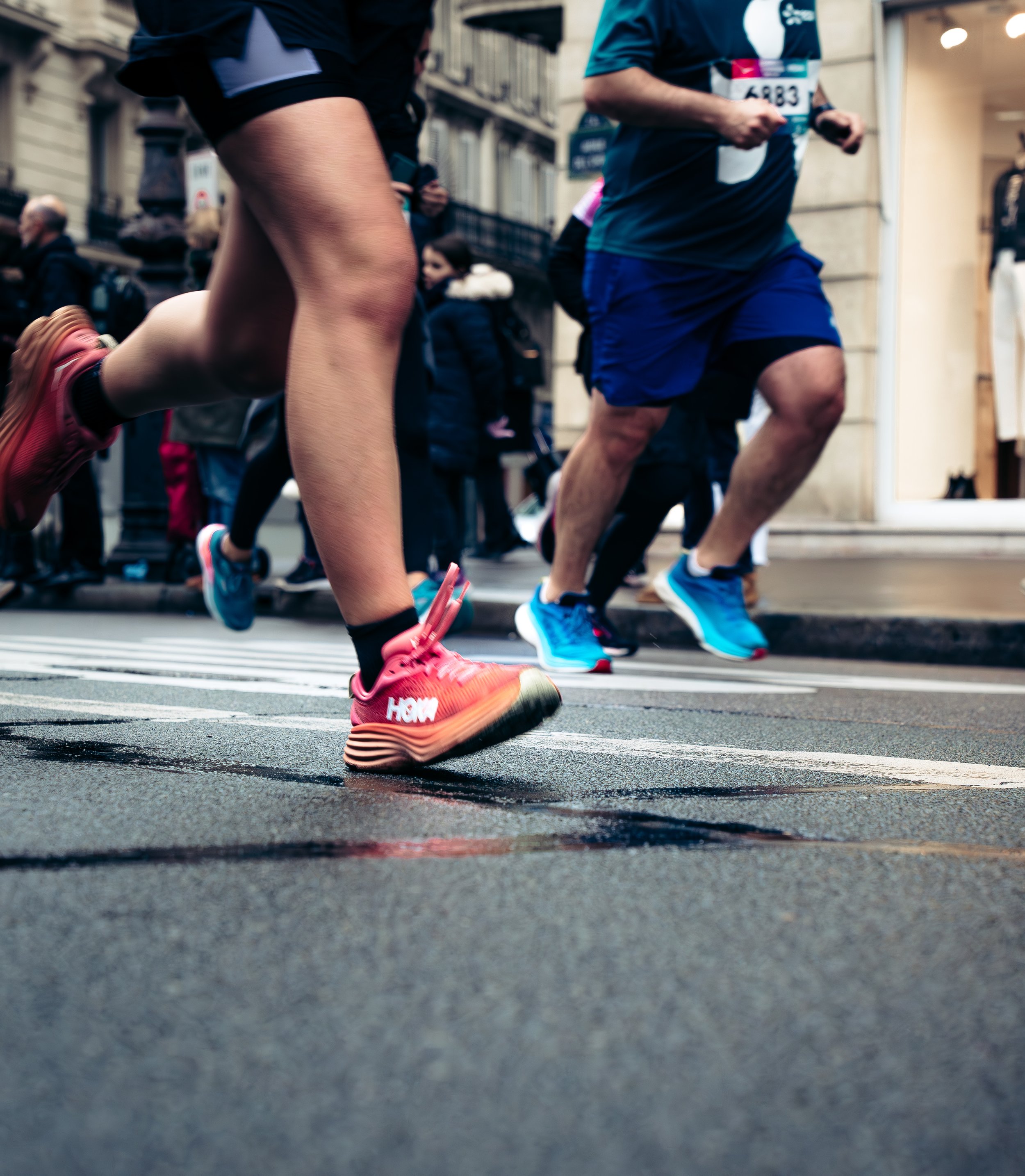 Close-up of runners' legs and feet during a marathon, with spectators in the background, on a city street.