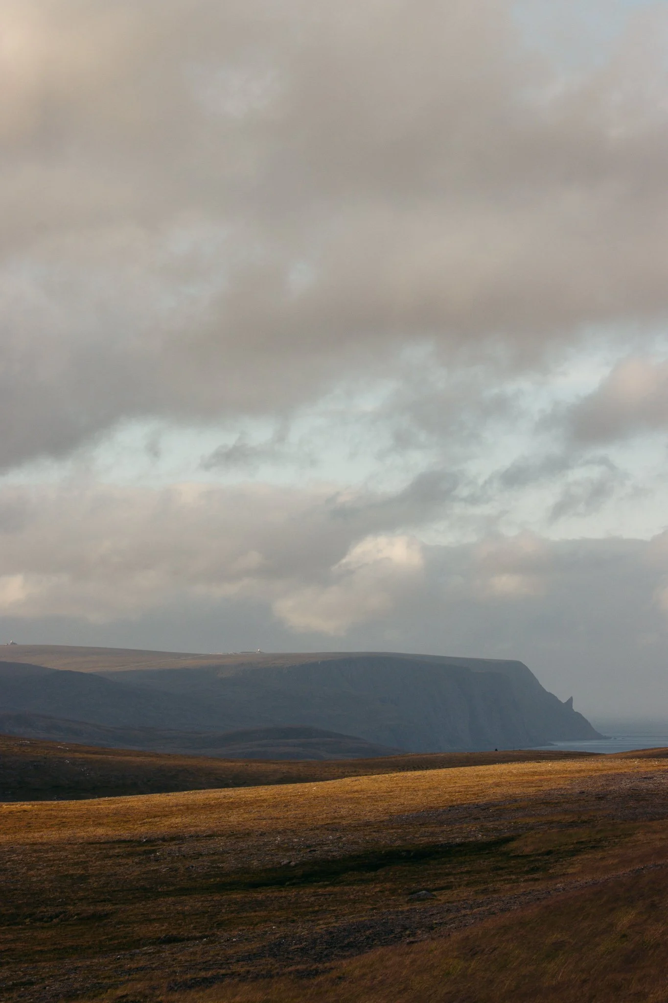 A landscape photo of a cloudy sky above rolling hills and a distant sea or ocean in the background.