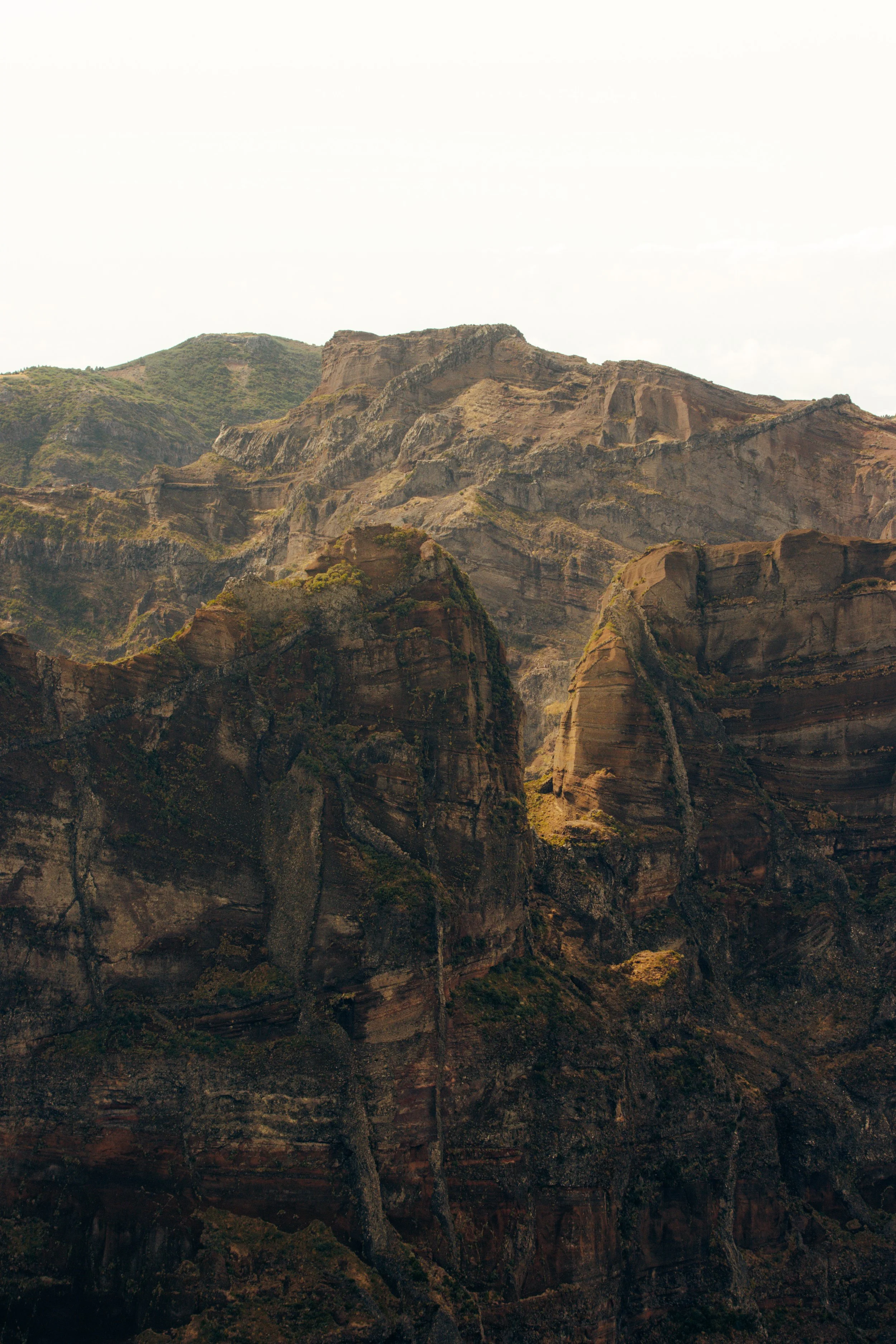 Landscape of rugged mountainous terrain with steep cliffs and layered rock formations under a cloudy sky.