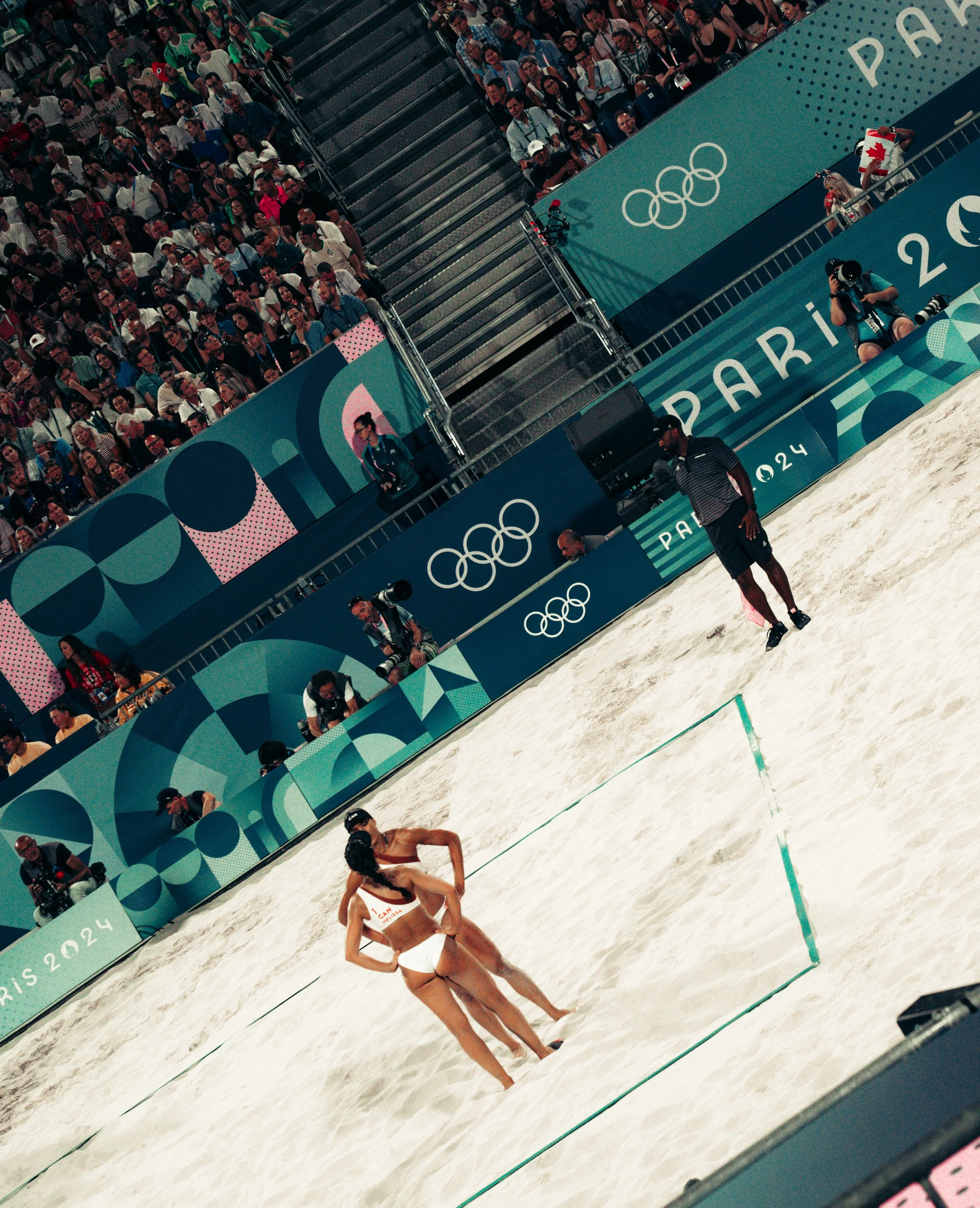 Olympic beach volleyball match at the 2024 Paris games with players, spectators, and Olympic branding.