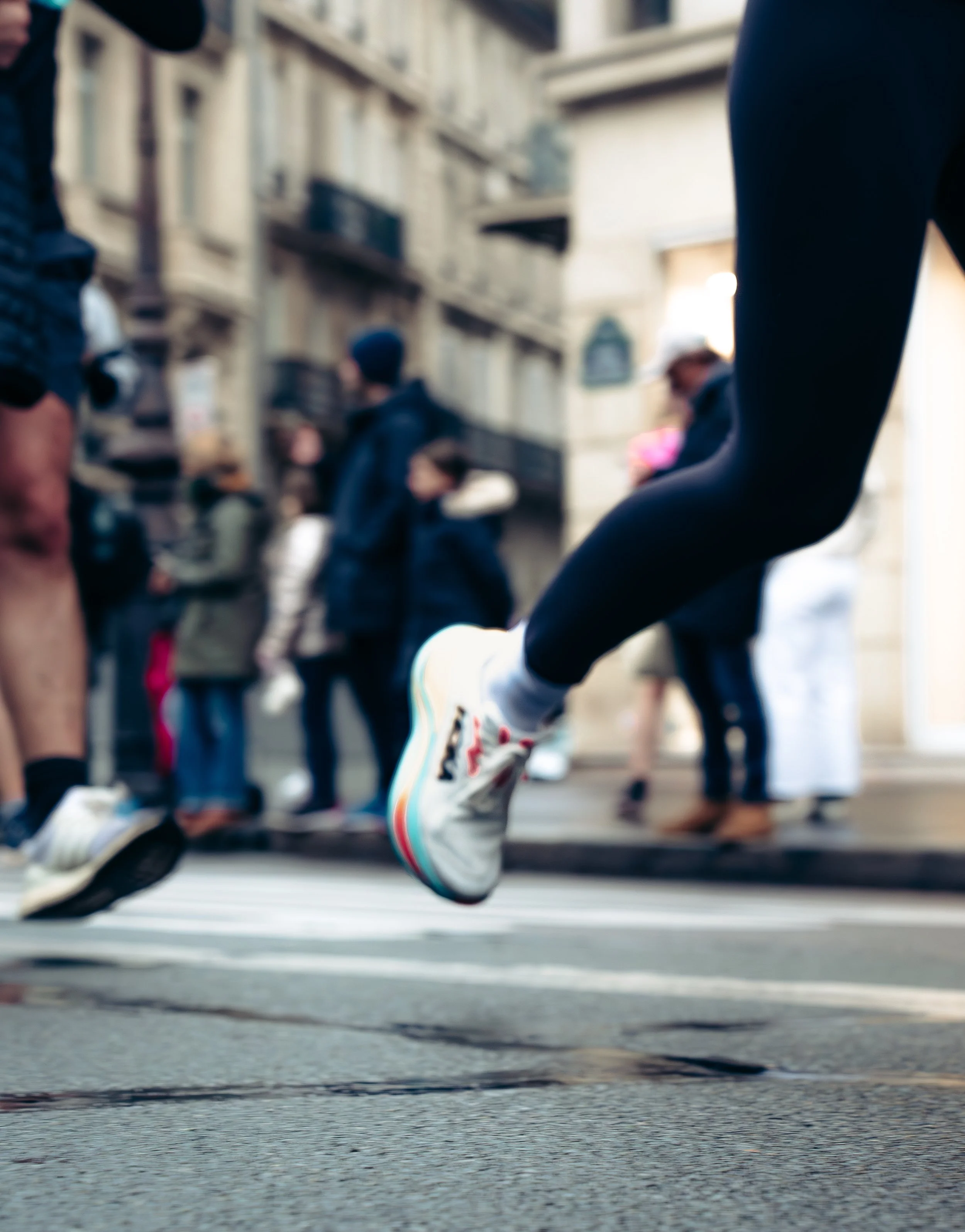 Close-up of a person running or jumping over a street crossing with other pedestrians and buildings in the background.