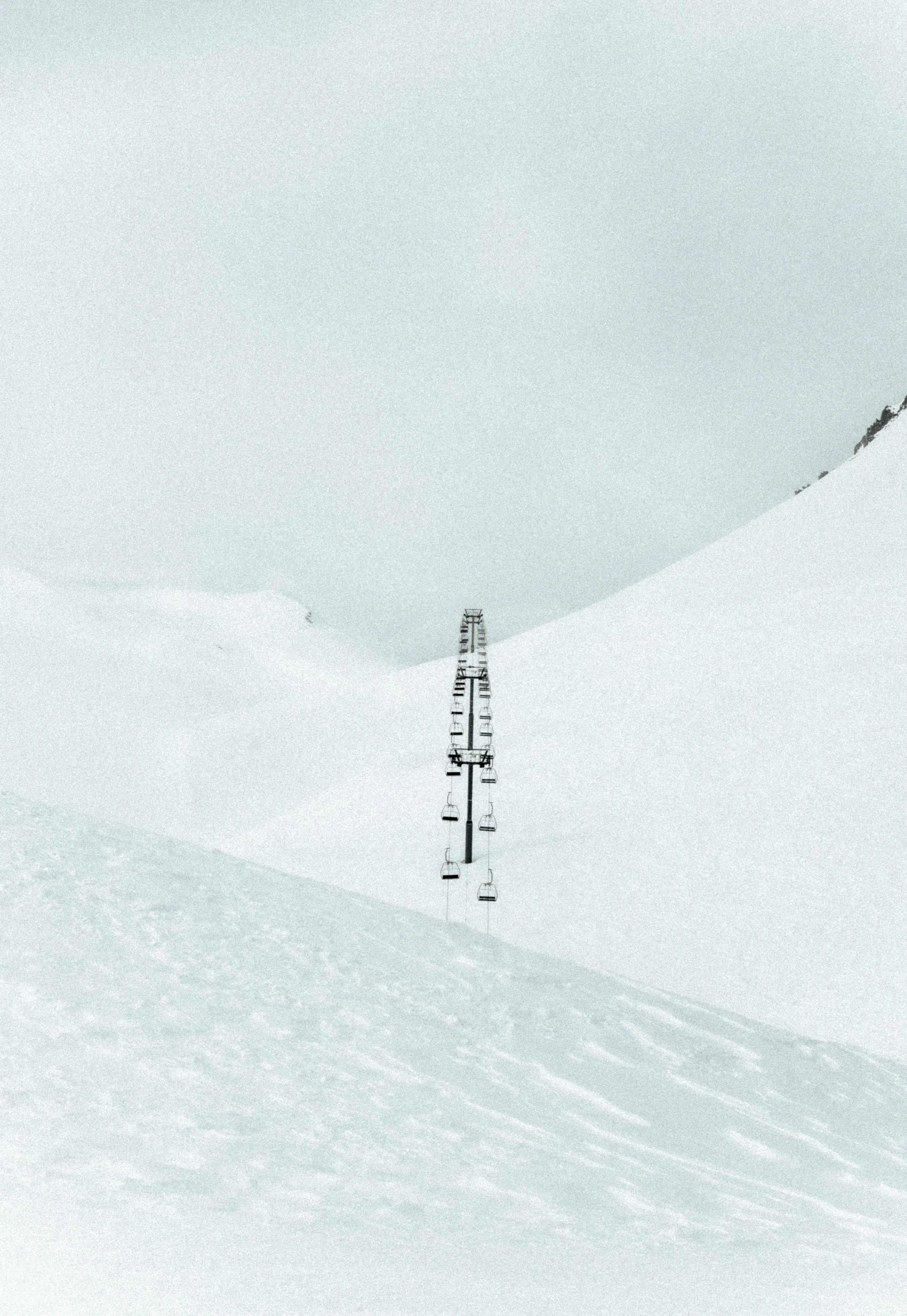 A ski lift ascending through a snow-covered mountain landscape with a light gray cloudy sky.