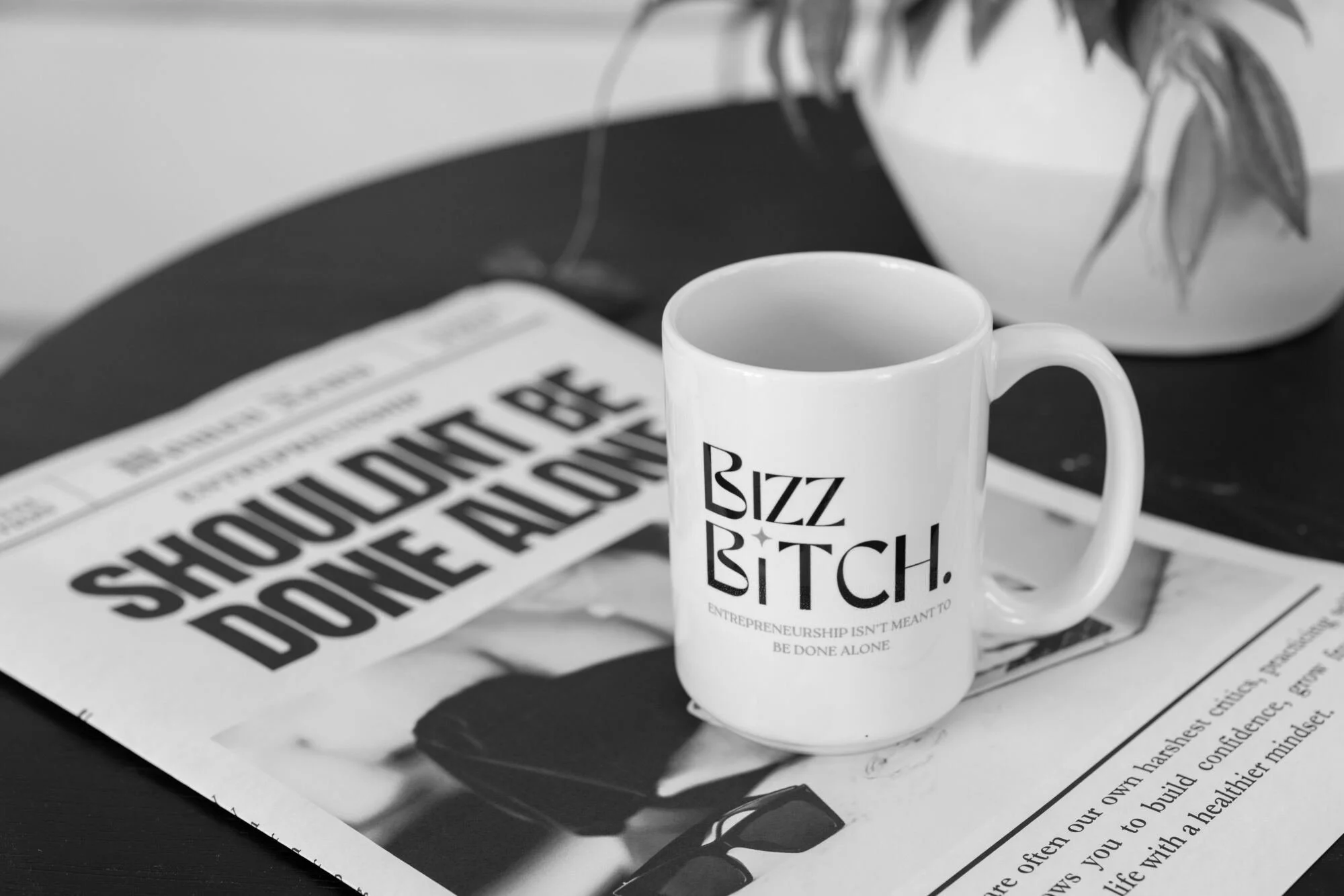 Bizz Bitch branded coffee mug placed on a magazine with entrepreneurship content, creating a modern workspace aesthetic focused on business, leadership, and female entrepreneurship.