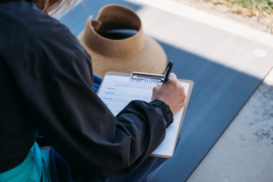 Entrepreneur writing notes on a clipboard outdoors, with a laptop and workspace essentials nearby, representing business planning, goal setting, productivity, and creative strategy.