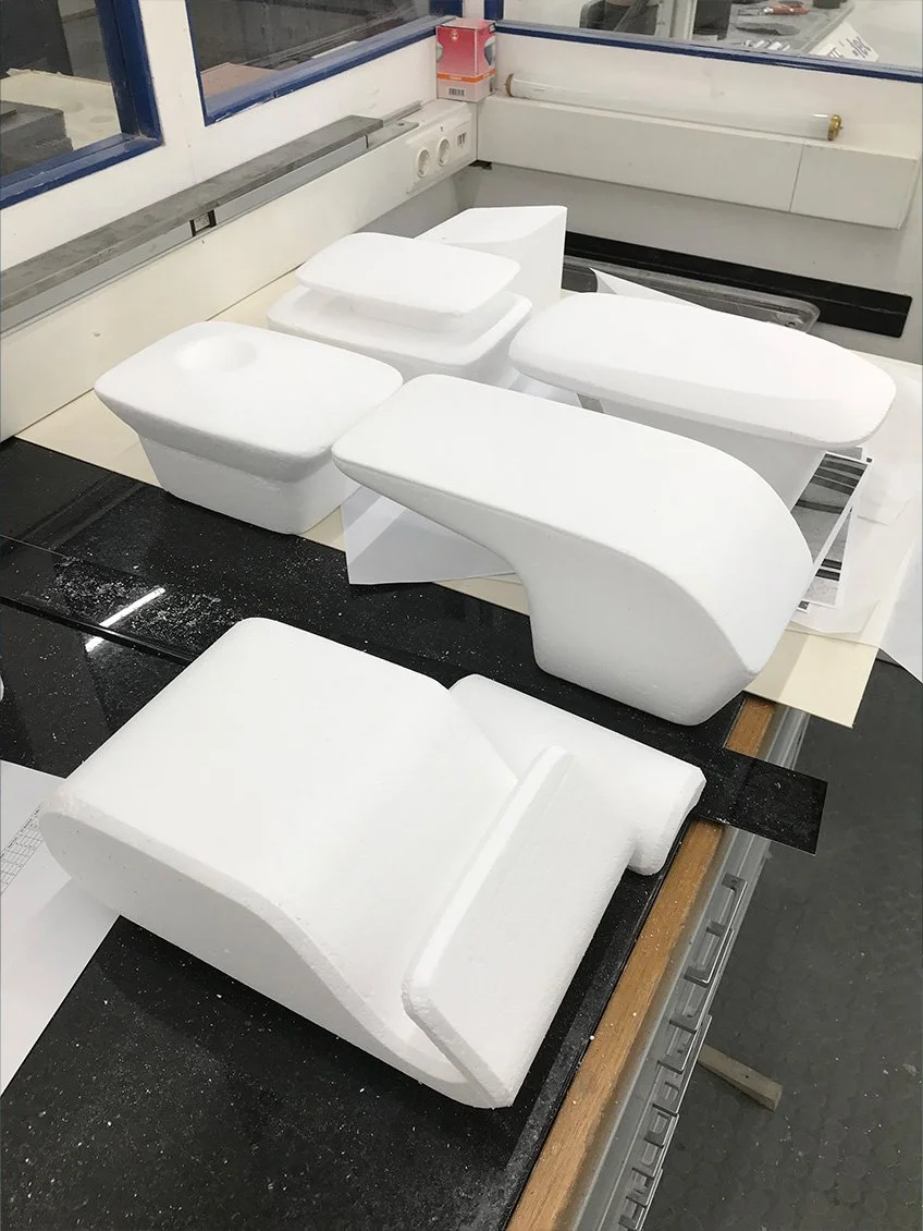 Weiß geformte Styropormodelle, die möglicherweise Möbel- oder Designprototypen darstellen, auf einem Werkbank in einer Werkstatt.