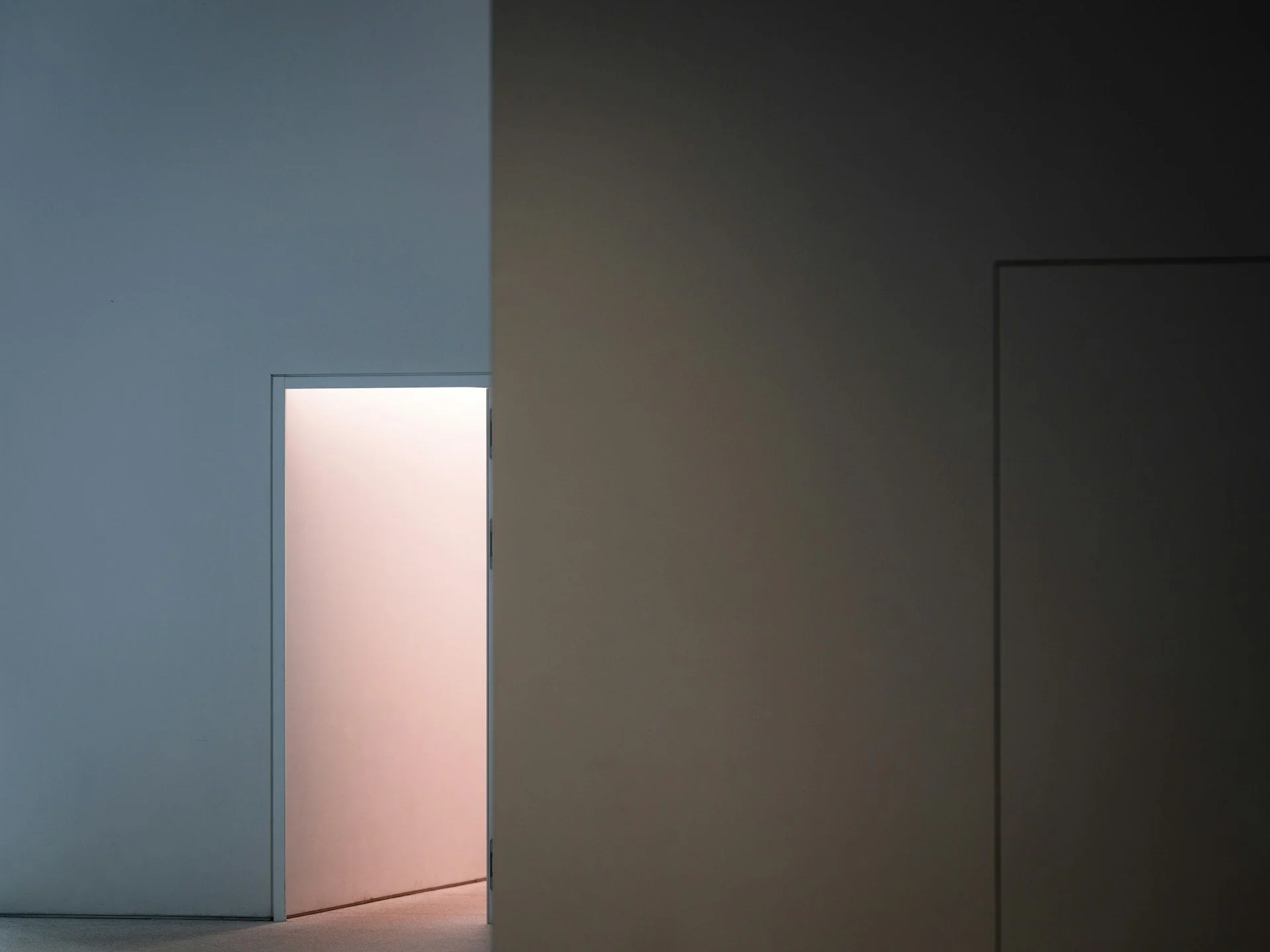 Ein heller, offener Raum mit einer Tür, durch die schwaches Licht einfällt. Die Wände sind in neutralen Farben gehalten, die Tür ist leicht geöffnet.