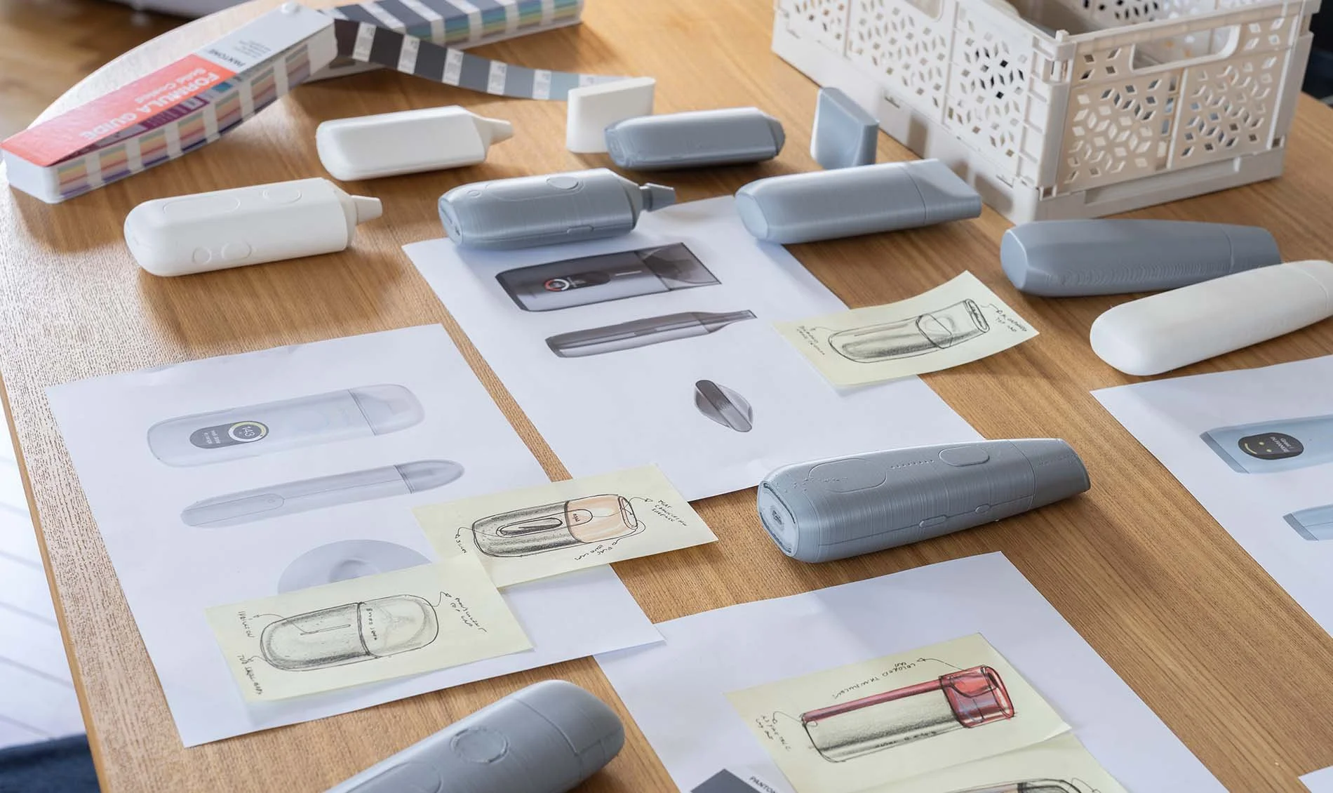 Entwicklungsprozess eines batteriebetriebenen Trinkbehälters, mit Skizzen, Prototypen und technischen Zeichnungen auf einem Holztisch.