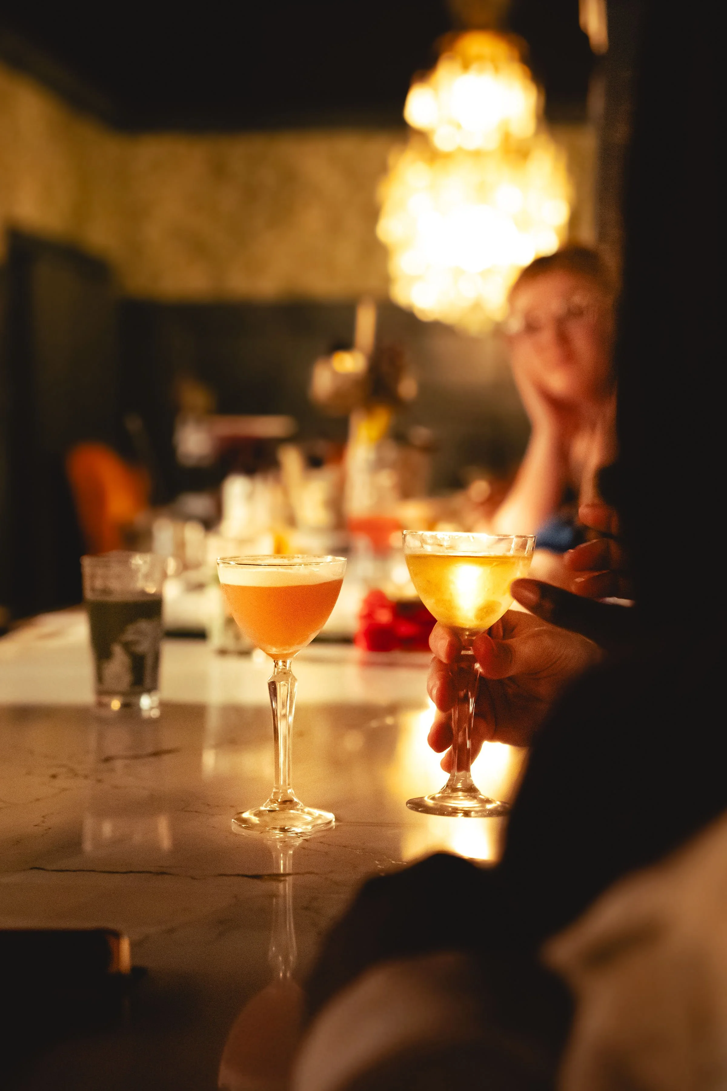 Guests enjoying vibrant amber and gold craft cocktails served in vintage coupe glasses in an intimate, candlelit lounge at 1854 in Cookeville.