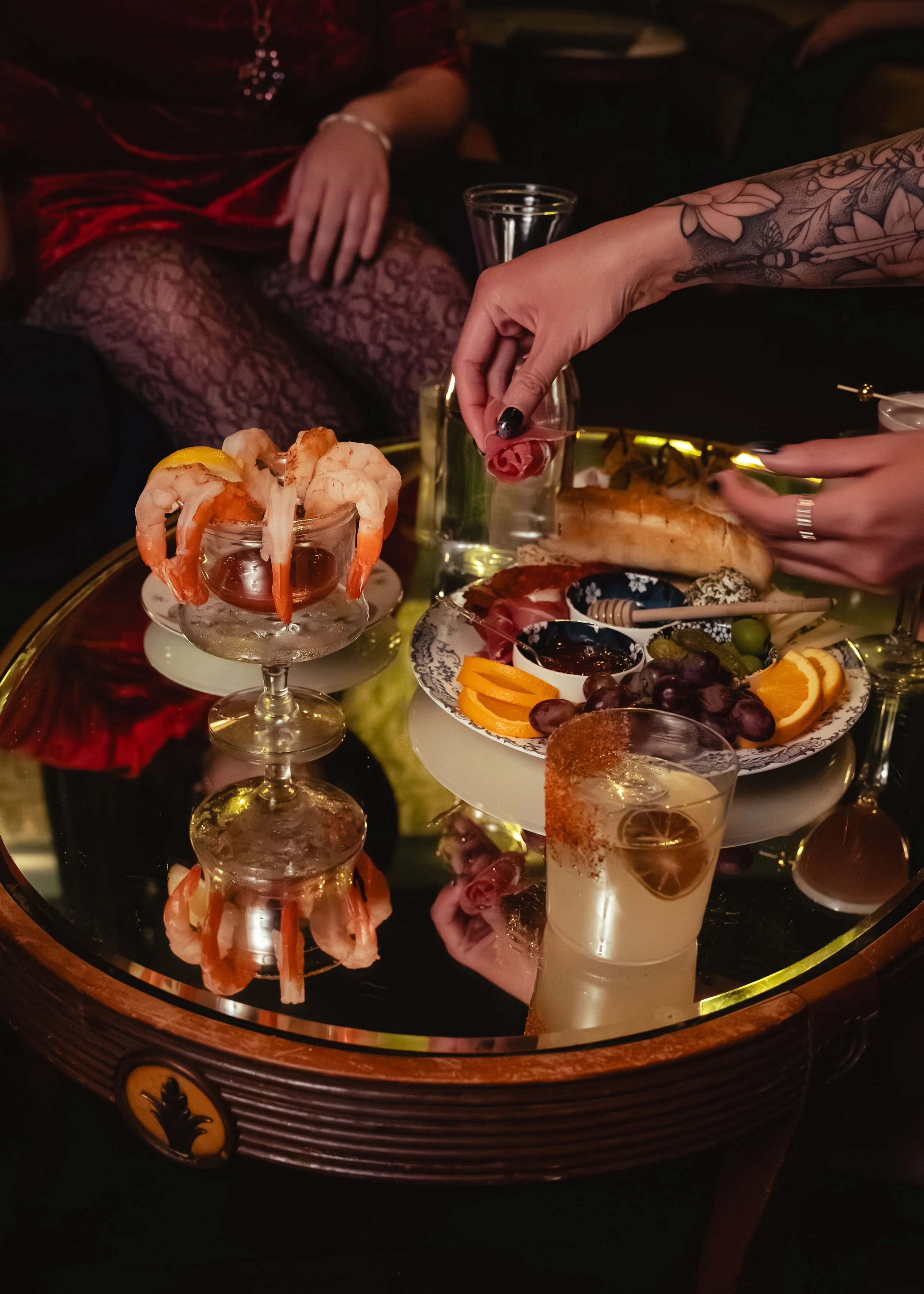 A beautifully styled, warm photo of an artisanal charcuterie board and specialty small plates alongside crystal cocktail glasses