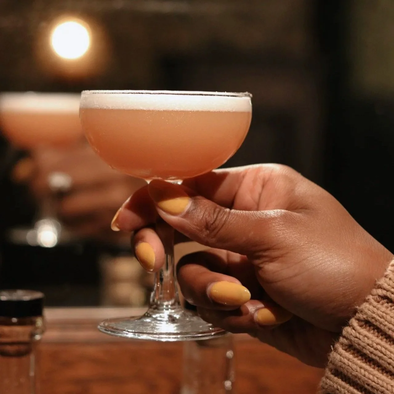 Guest holding a handcrafted seasonal craft cocktail in an elegant coupe glass at 1854 Cocktail Bar & Lounge in Cookeville TN.