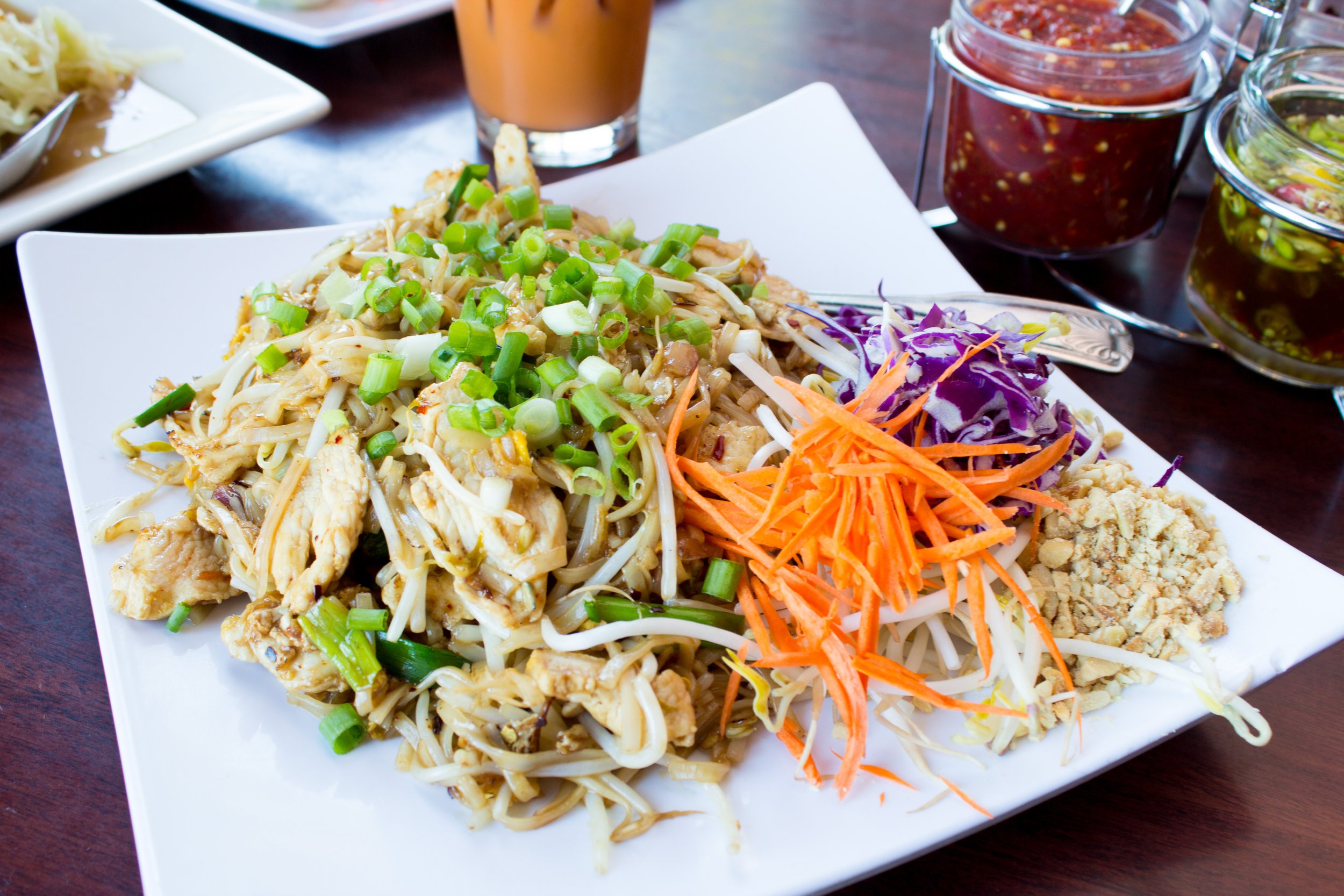 Chicken Pad Thai on a white plate garnished with green onions and carrots