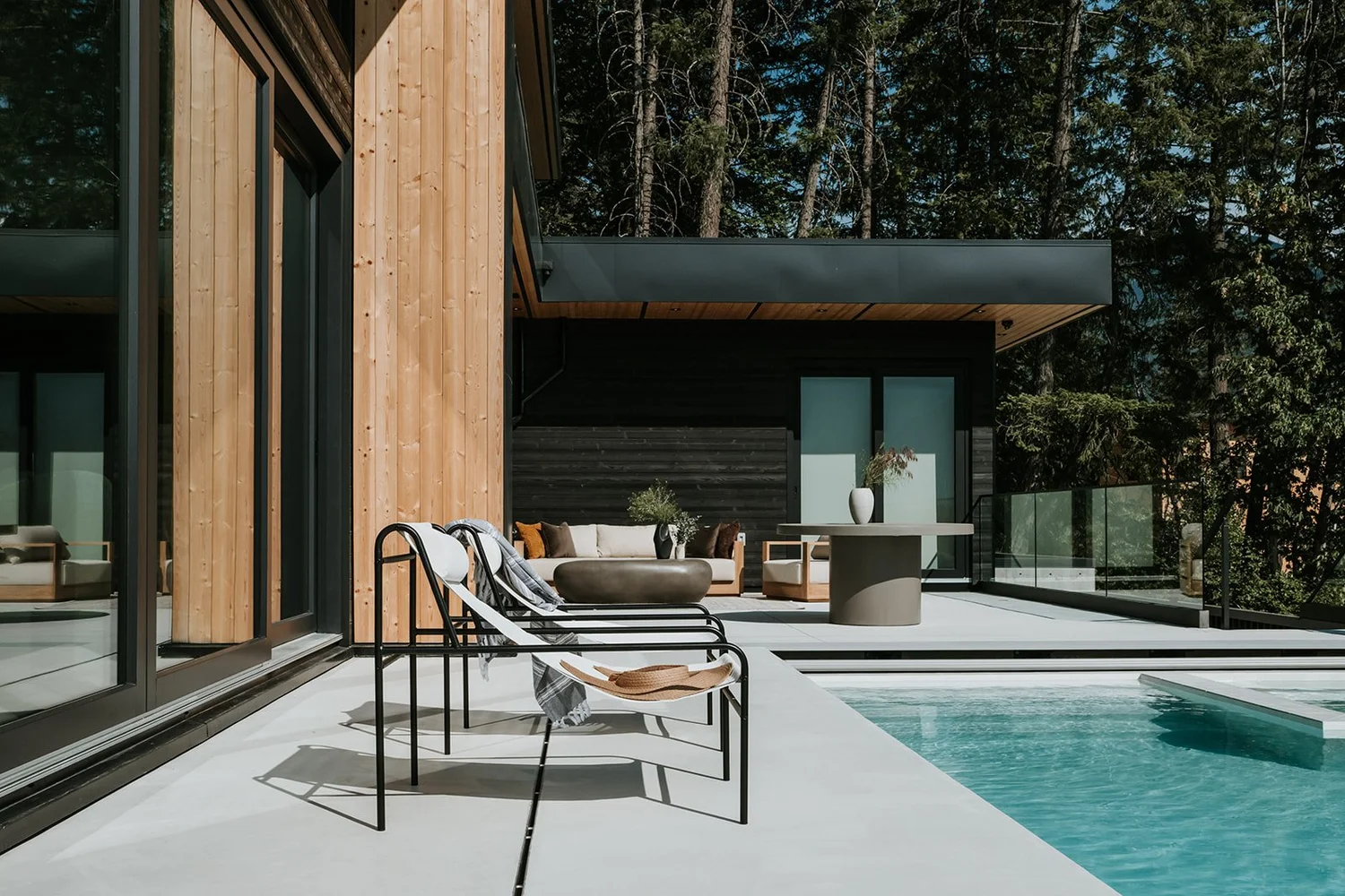 Sunstone Outdoor living area with pool, cedar cladding, glass walls, modern outdoor furniture — new-build interior design in Pemberton, BC by LRD Studio. Photography by Darby Magill.