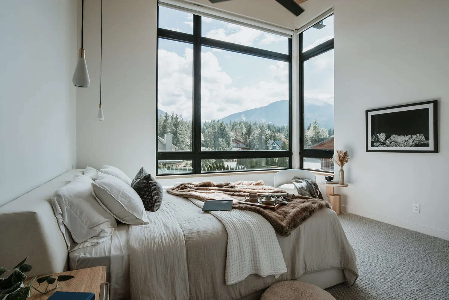 Balsam Mountain view through large corner windows, pendant light, grey upholstered bed — new-build interior design in Whistler, BC by LRD Studio. Photography by Darby Magill.