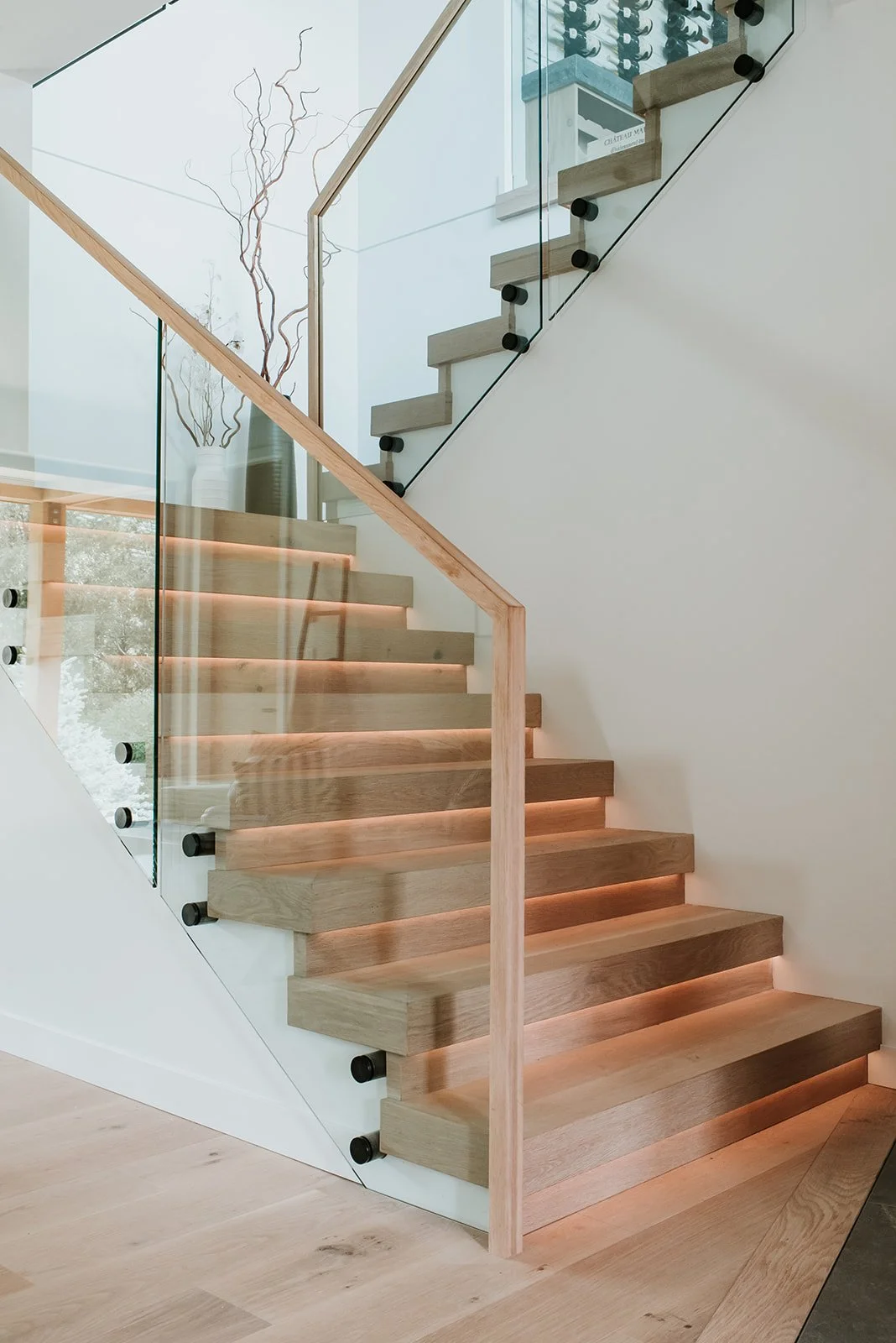 Balsam Oak stairs with underlit risers (warm glow), glass railing with black mounts — new-build interior design in Whistler, BC by LRD Studio. Photography by Darby Magill.