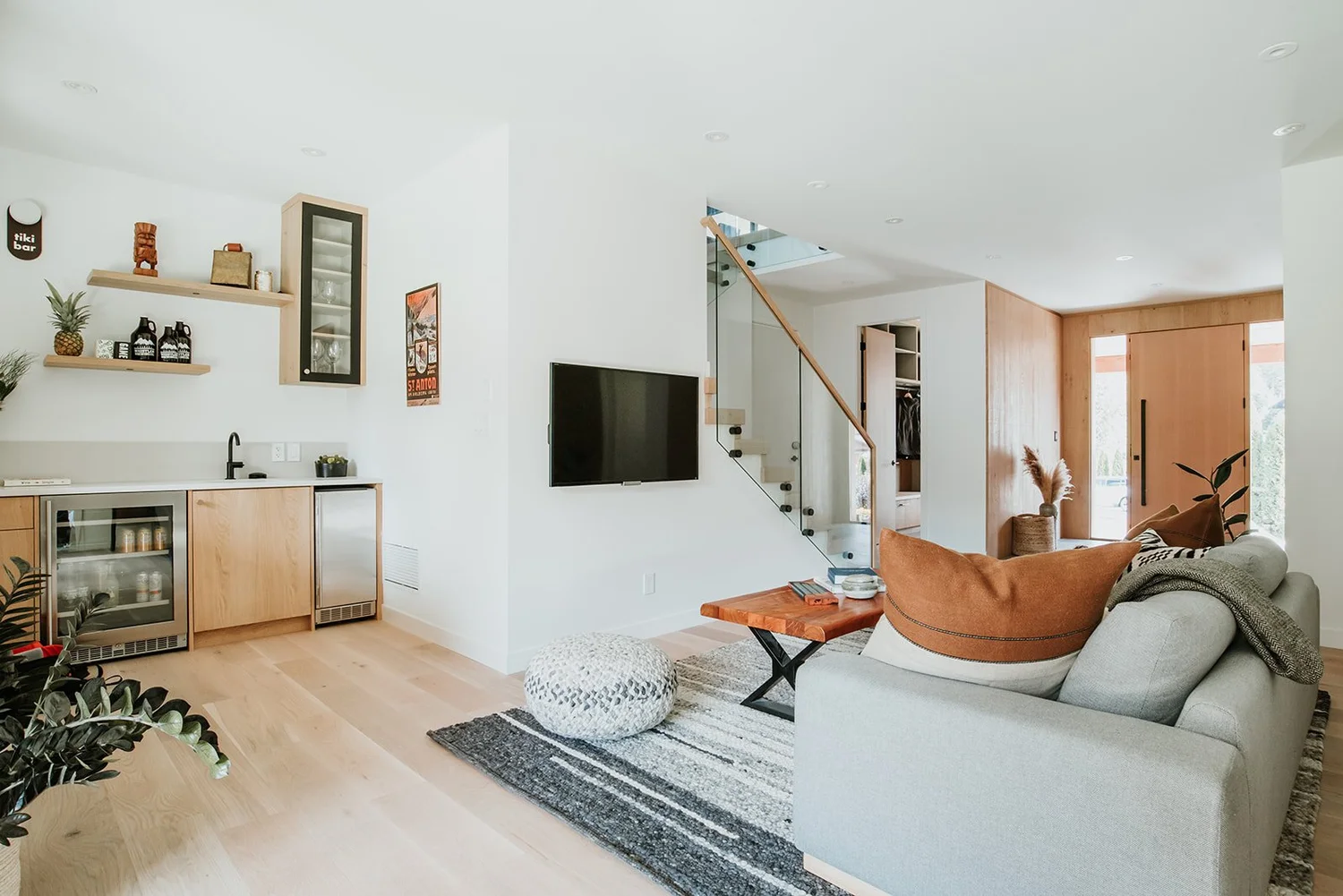 Balsam Full media room: tiki bar left, TV on wall, glass staircase, concealed closet door — new-build interior design in Whistler, BC by LRD Studio. Photography by Darby Magill.