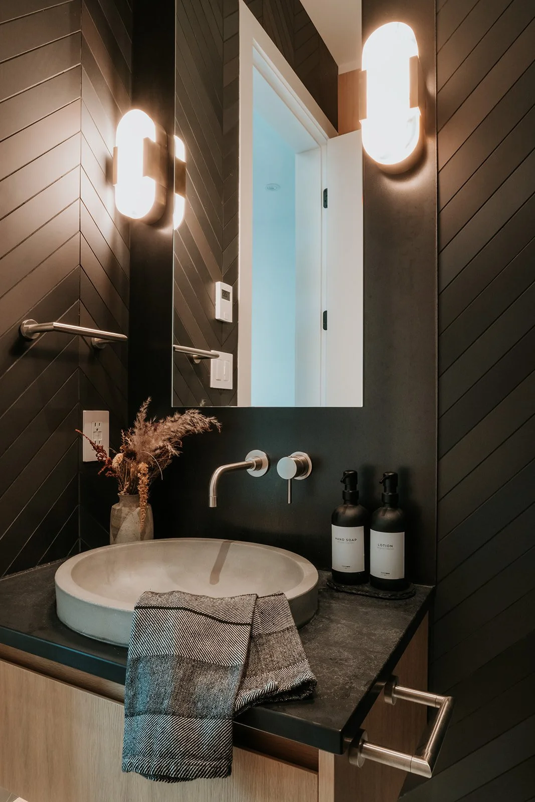 Sunstone Powder room straight-on: oval sconces, chevron tile with irregular texture, vessel sink — new-build interior design in Pemberton, BC by LRD Studio. Photography by Darby Magill.