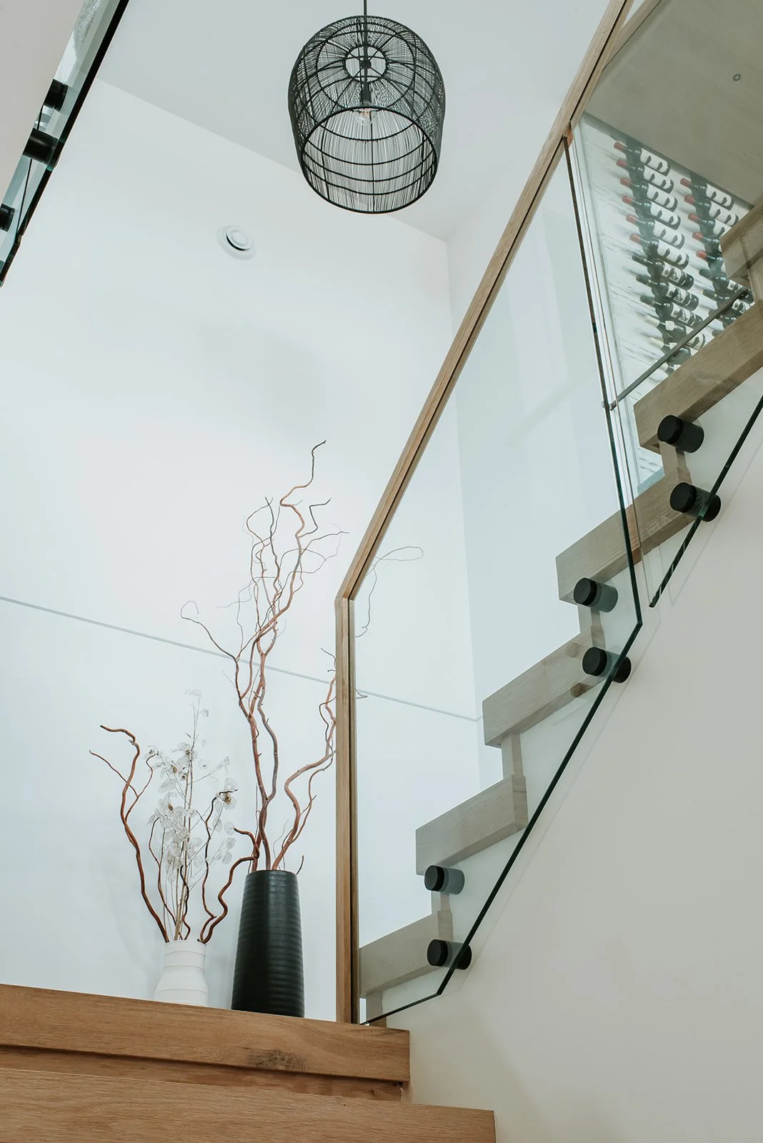 Balsam Looking up stairwell: basket-woven pendant, glass railing, dried branch arrangement — new-build interior design in Whistler, BC by LRD Studio. Photography by Darby Magill.