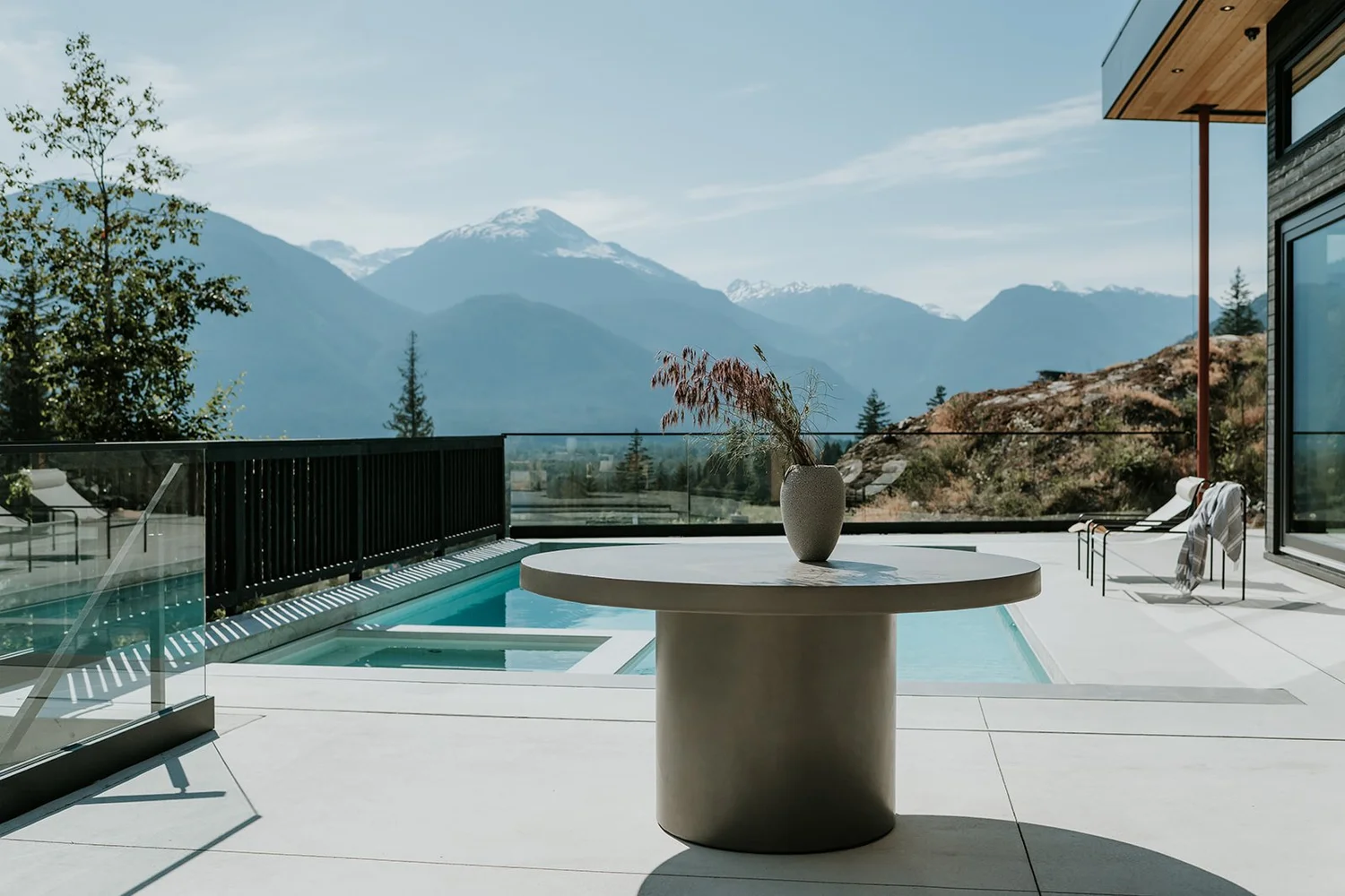 Sunstone Pool terrace with concrete round table, hot tub, full Pemberton valley panorama — new-build interior design in Pemberton, BC by LRD Studio. Photography by Darby Magill.