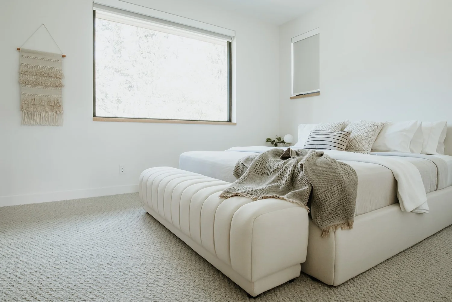 Balsam White channeled upholstered bed, macrame wall hanging, minimal neutral palette — new-build interior design in Whistler, BC by LRD Studio. Photography by Darby Magill.