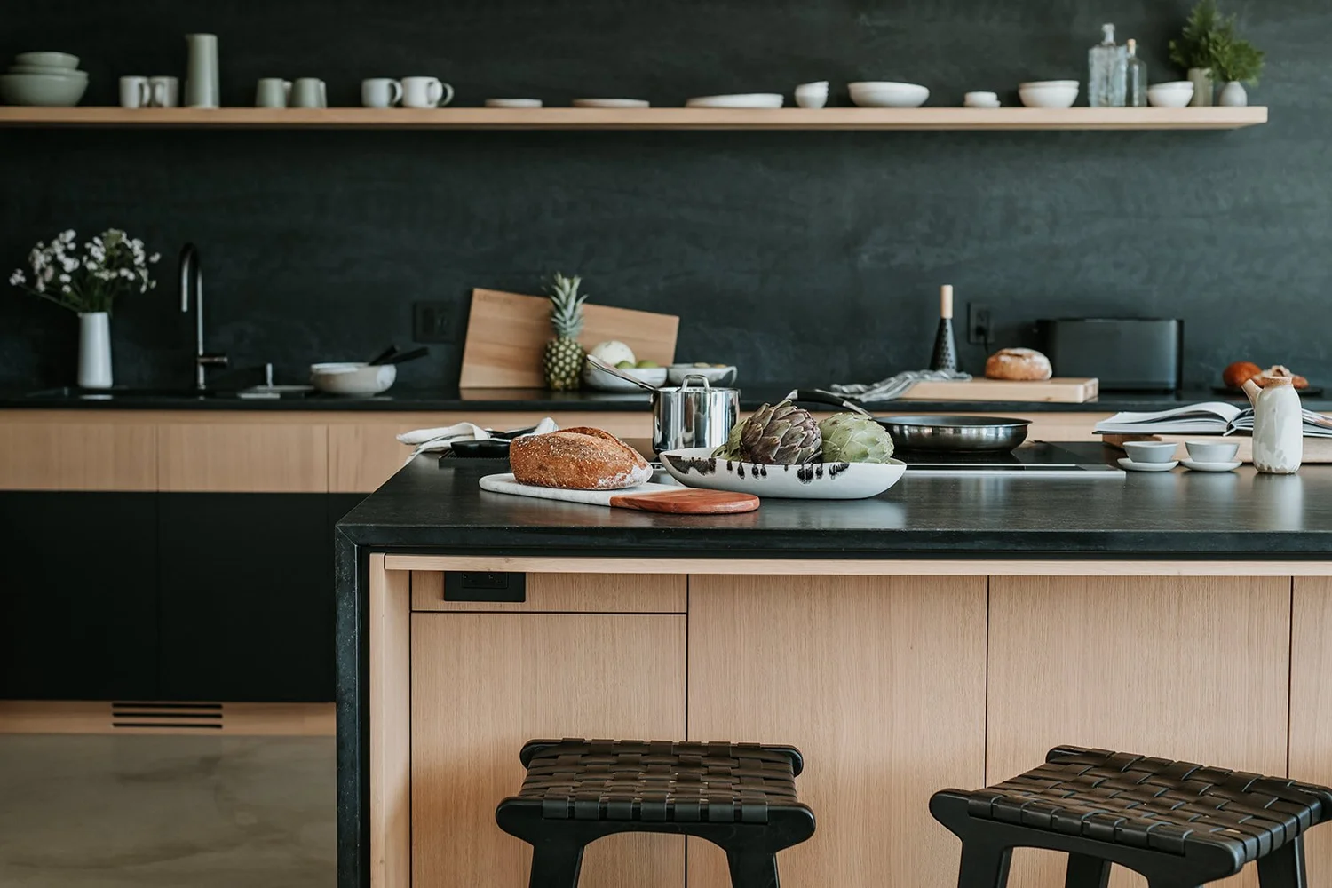 Sunstone Kitchen island with dark stone waterfall, woven leather stools — new-build interior design in Pemberton, BC by LRD Studio. Photography by Darby Magill.