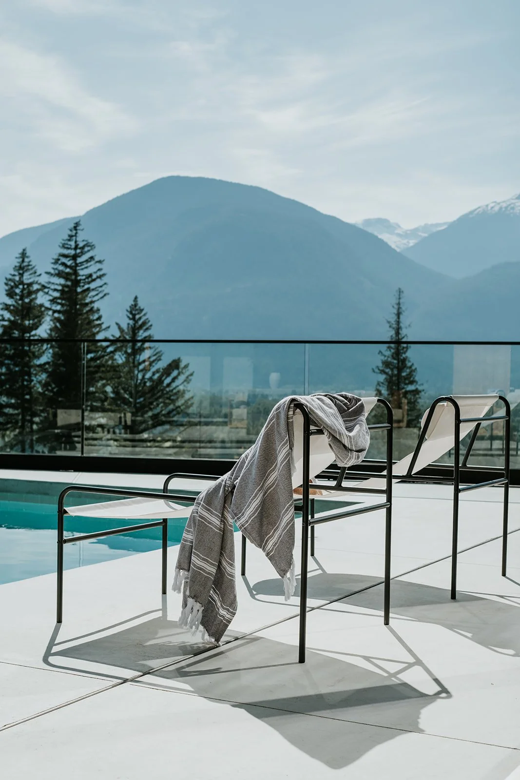 Sunstone Pool lounge chair with draped towel, snow-capped mountain panorama — new-build interior design in Pemberton, BC by LRD Studio. Photography by Darby Magill.