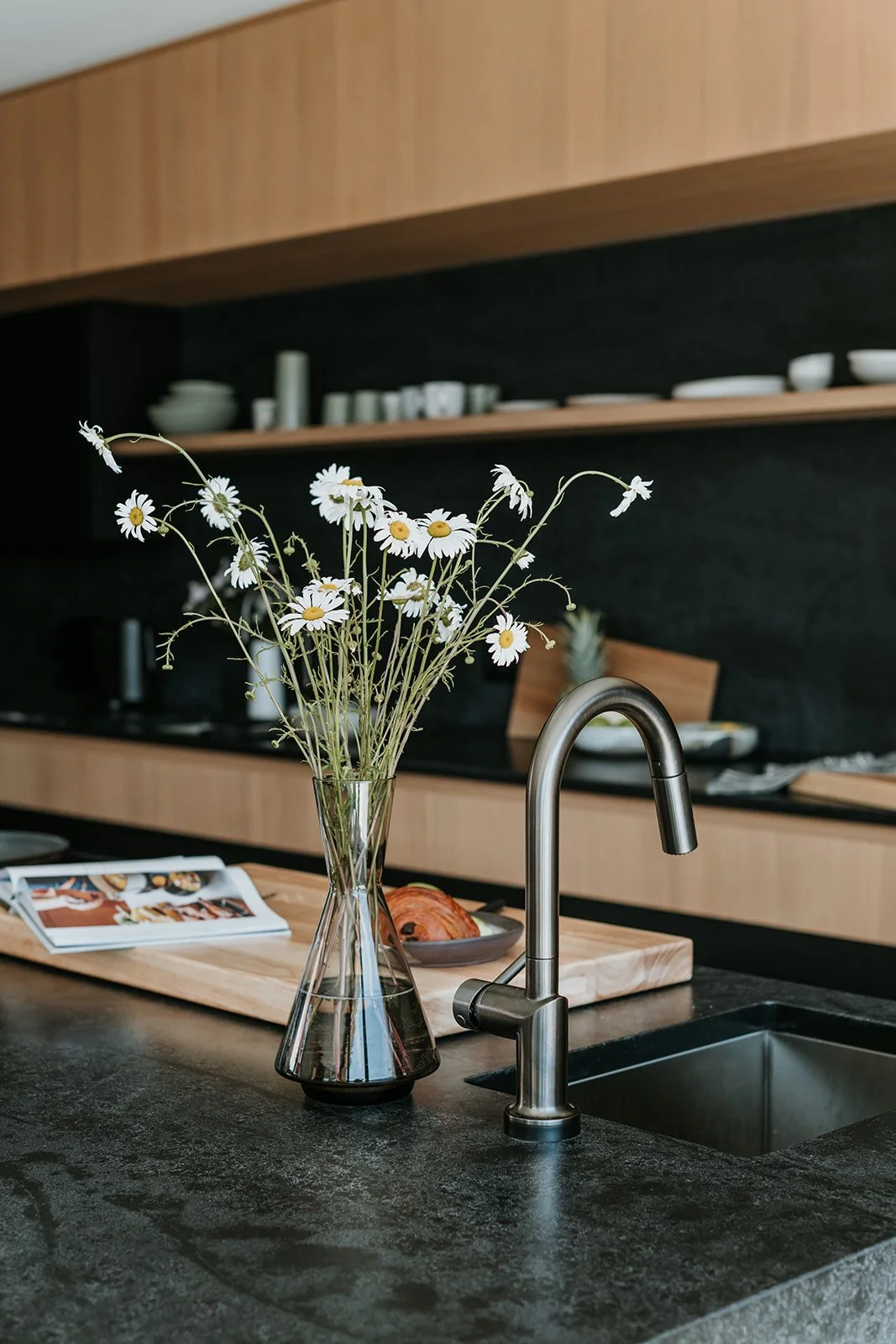Sunstone Kitchen sink with dark stone countertop, long exposed shelf with everyday dishes — new-build interior design in Pemberton, BC by LRD Studio. Photography by Darby Magill.